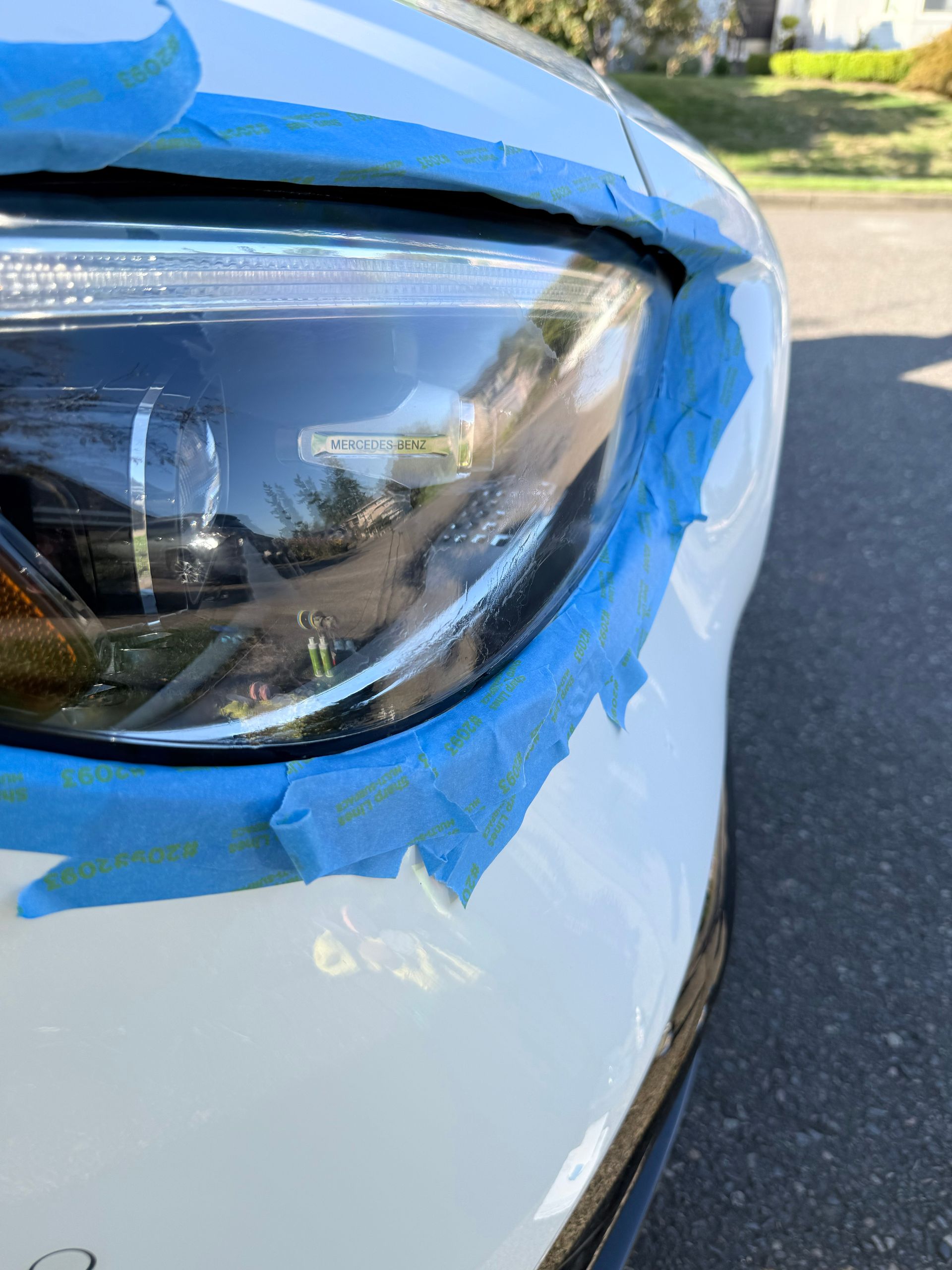 Close-up of a white car headlight with blue painter’s tape around the edge