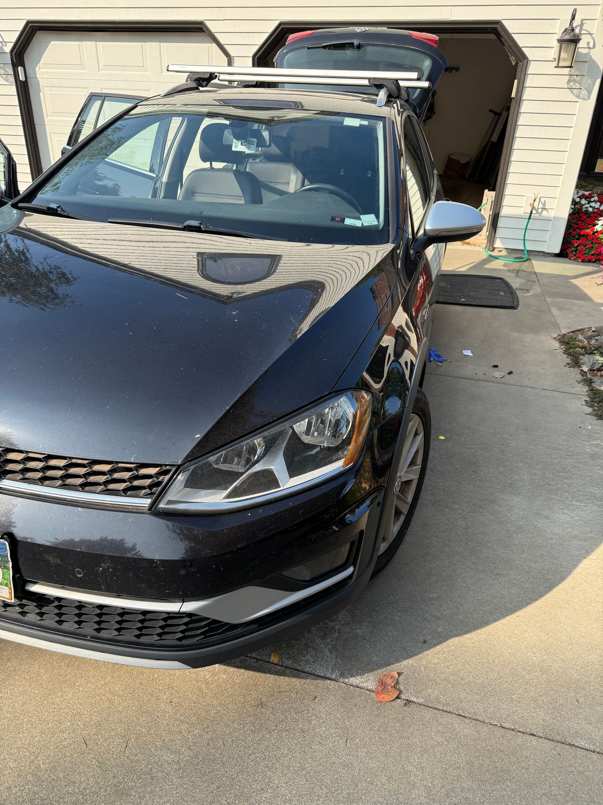 Black car parked in a driveway in front of a garage, with the trunk open.