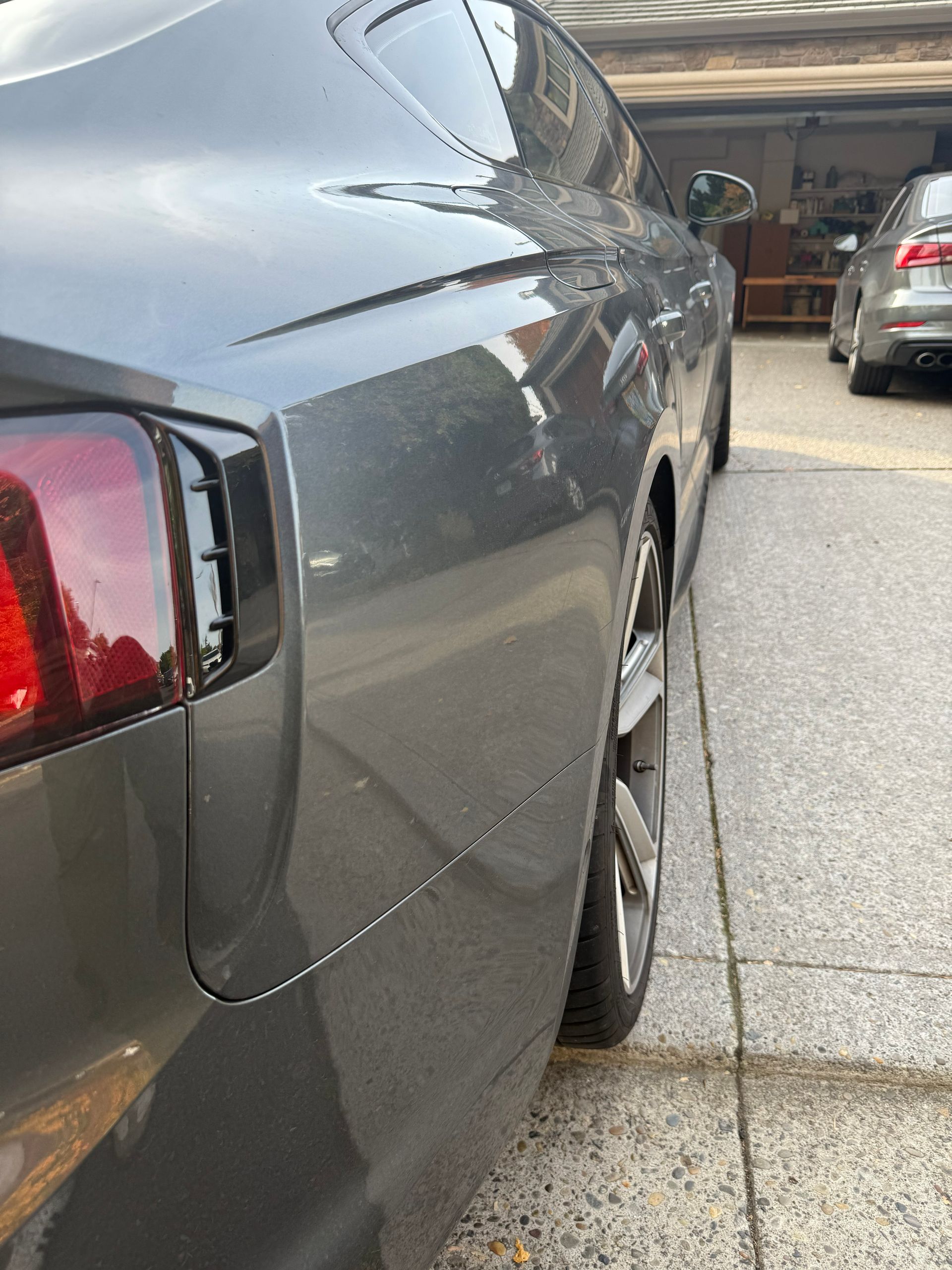 Gray car with rear damage and a dented side panel in a driveway/garage area