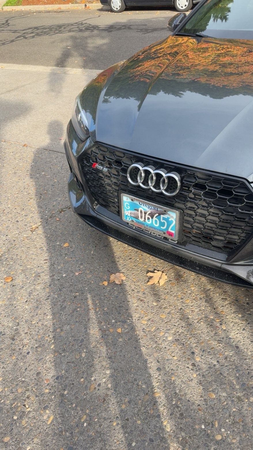 Front of a black Audi parked on a street, showing a damaged front bumper and license plate.