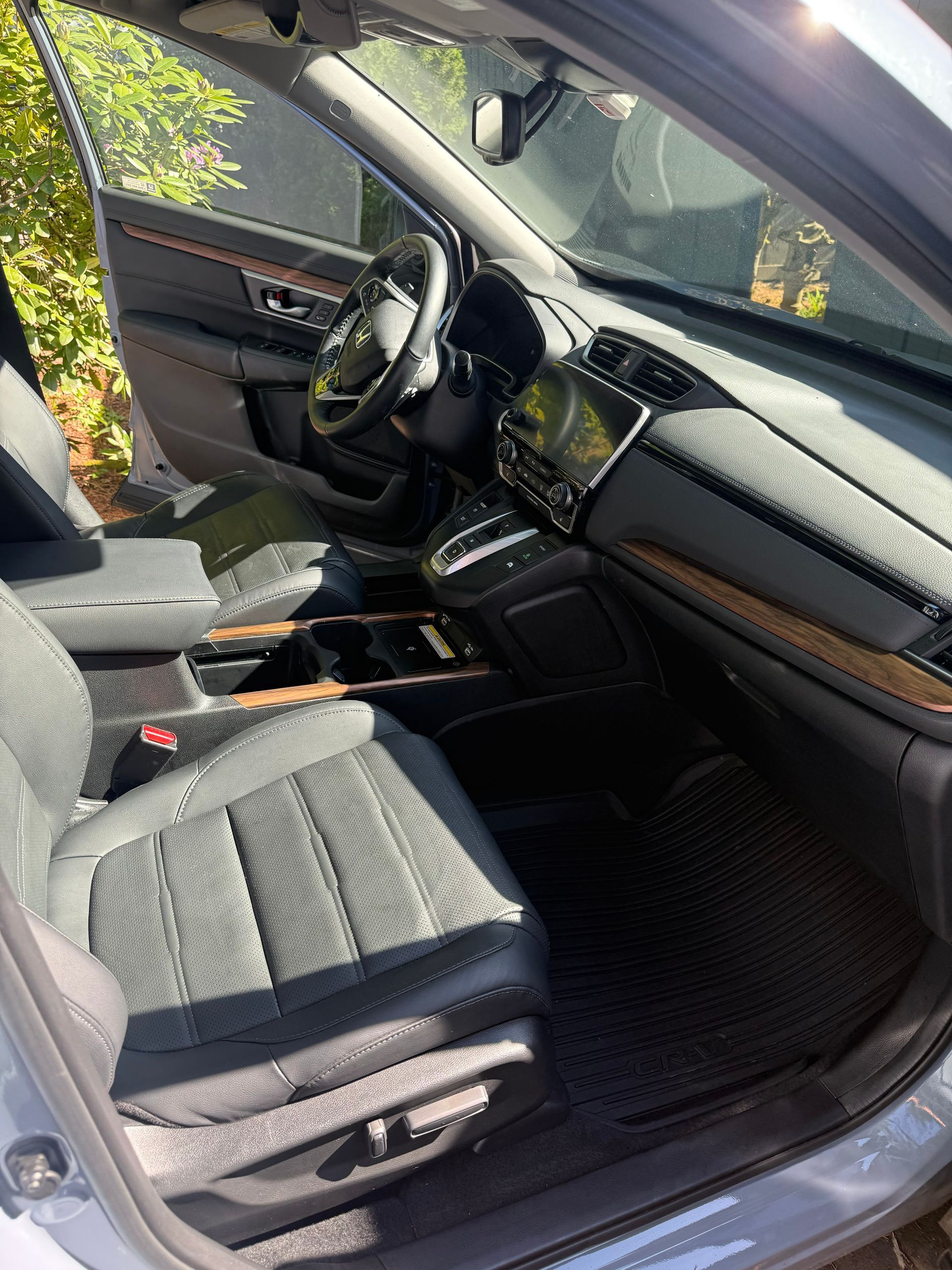 Car interior with black cloth seats, dashboard, and steering wheel, sunlit through the open driver’s door
