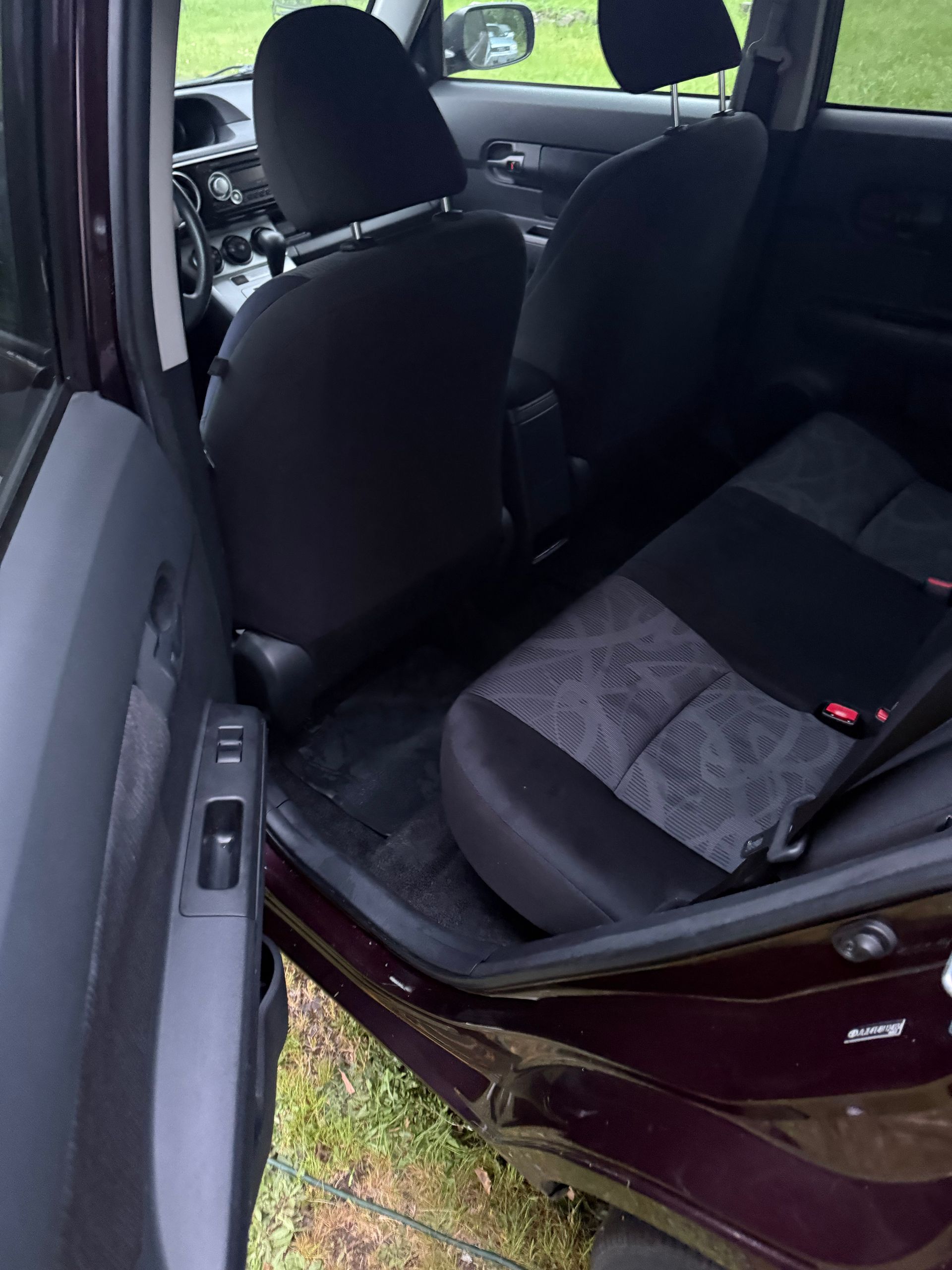 Open car door showing the front and rear seats of a maroon vehicle.