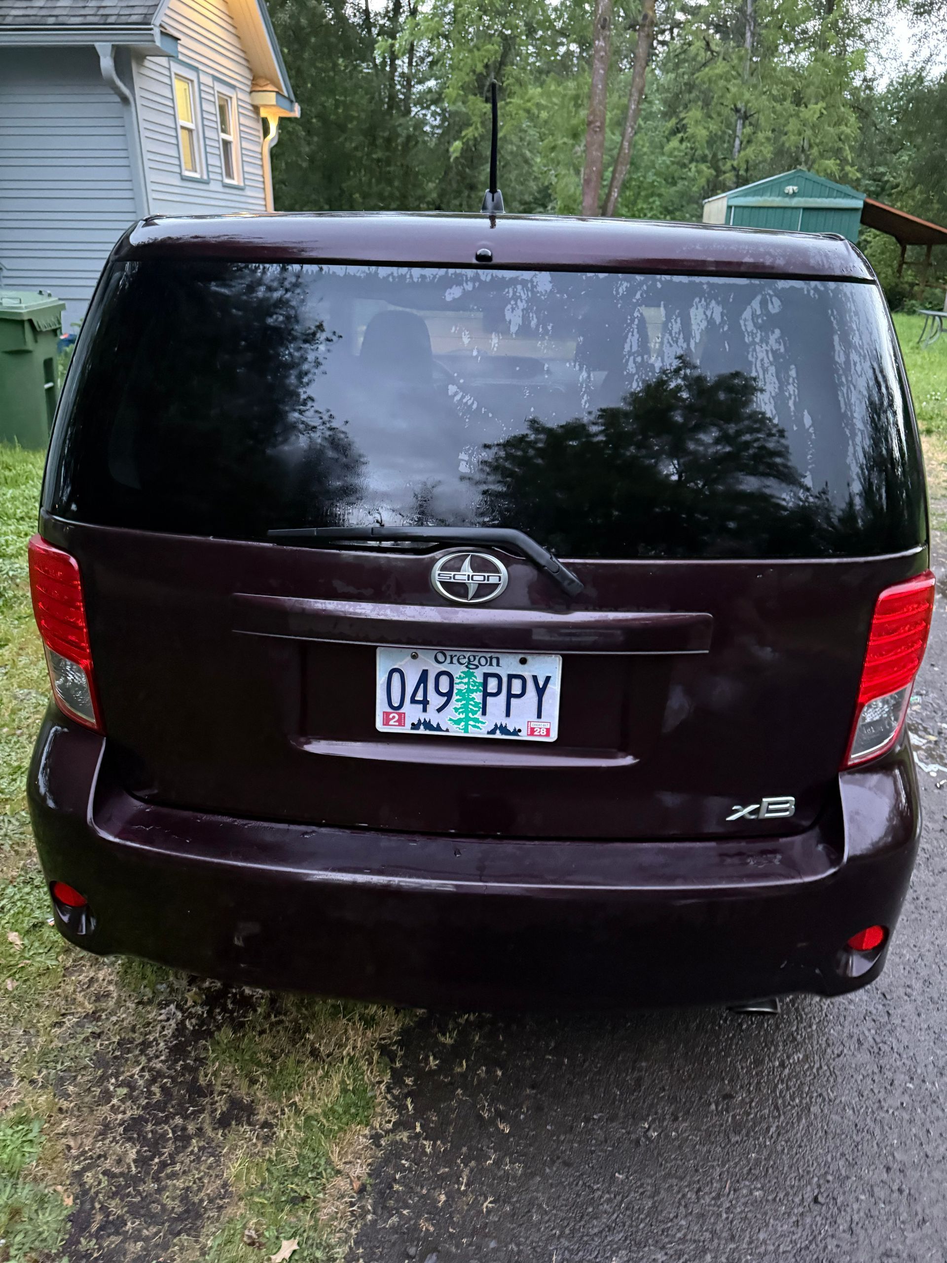 Dark maroon minivan parked in a narrow driveway with a license plate visible.