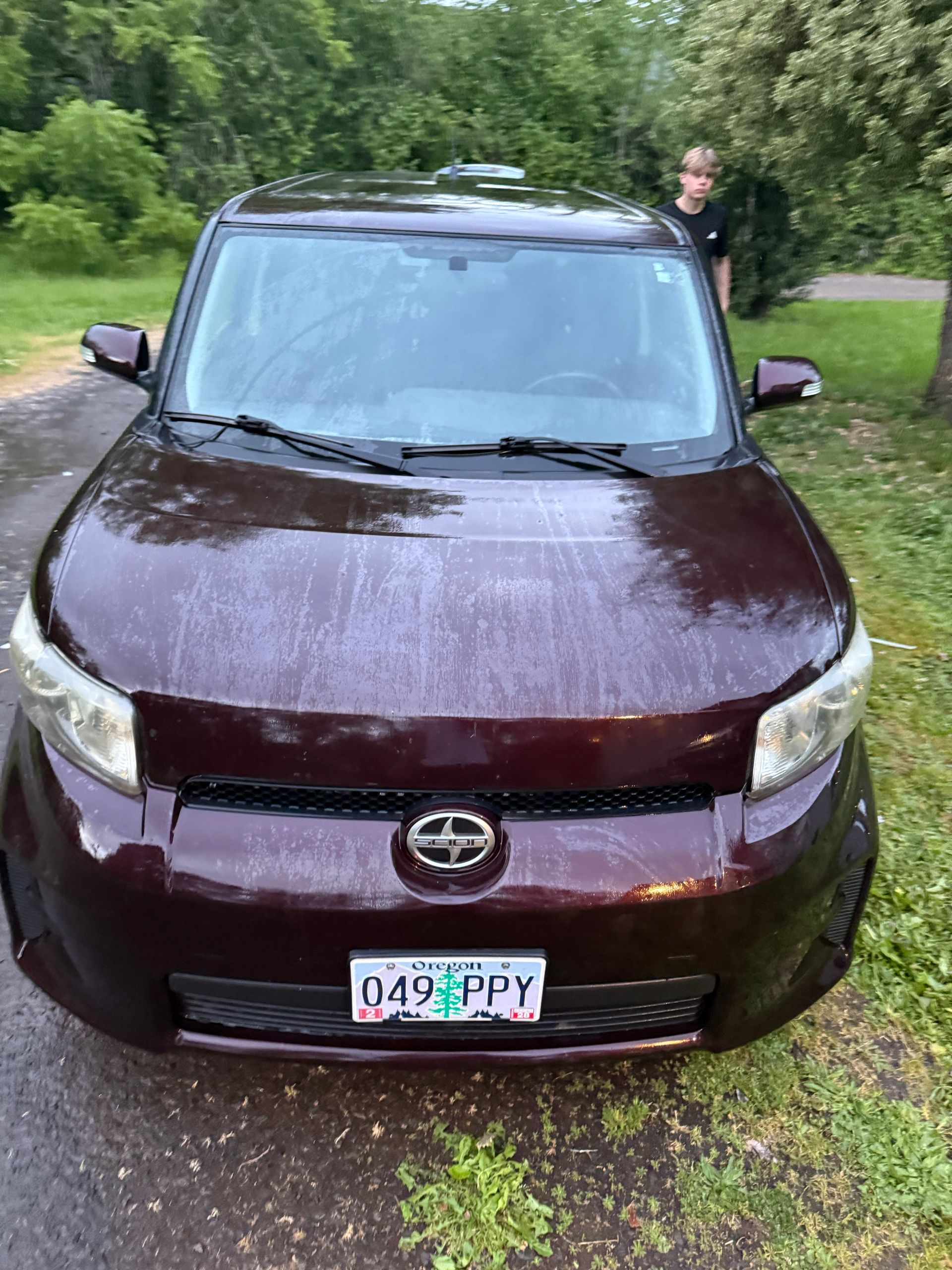 Maroon Toyota SUV parked on a gravel driveway, with a person standing behind it near trees.