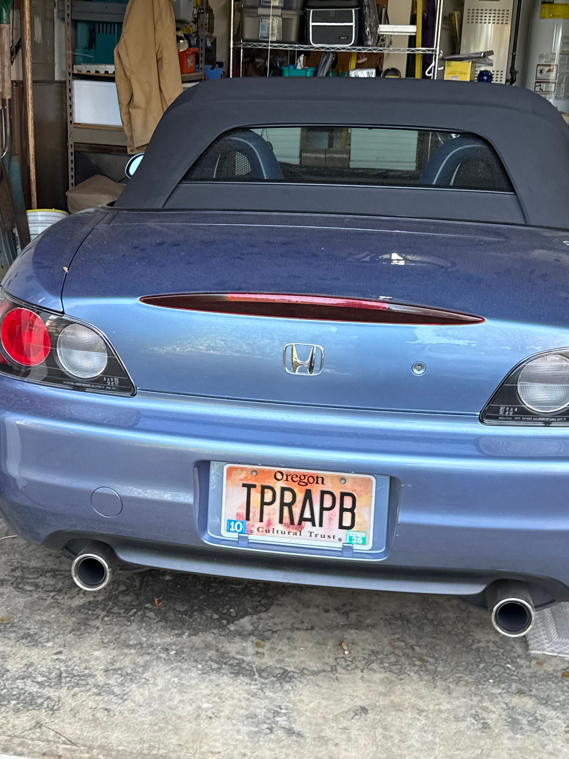 Blue Honda S2000 convertible parked in a garage, rear view with personalized license plate.