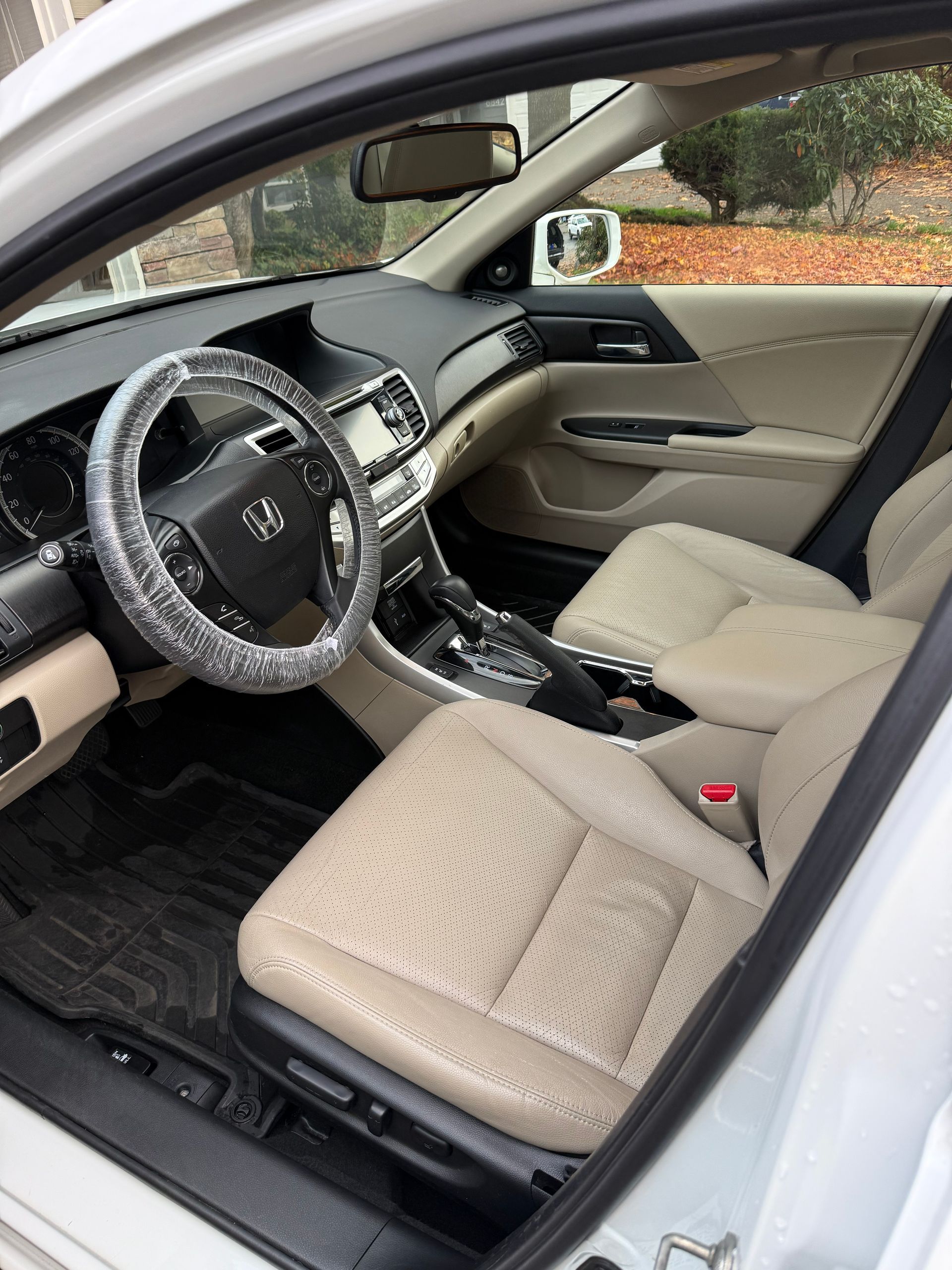 Car interior with beige seats, black steering wheel, and dashboard, viewed through the open driver’s door