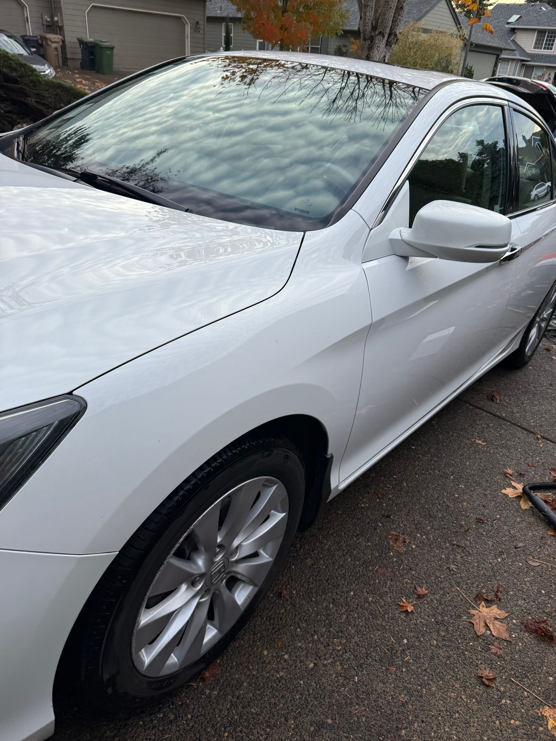White sedan parked on a wet street beside a building, viewed from the front side.