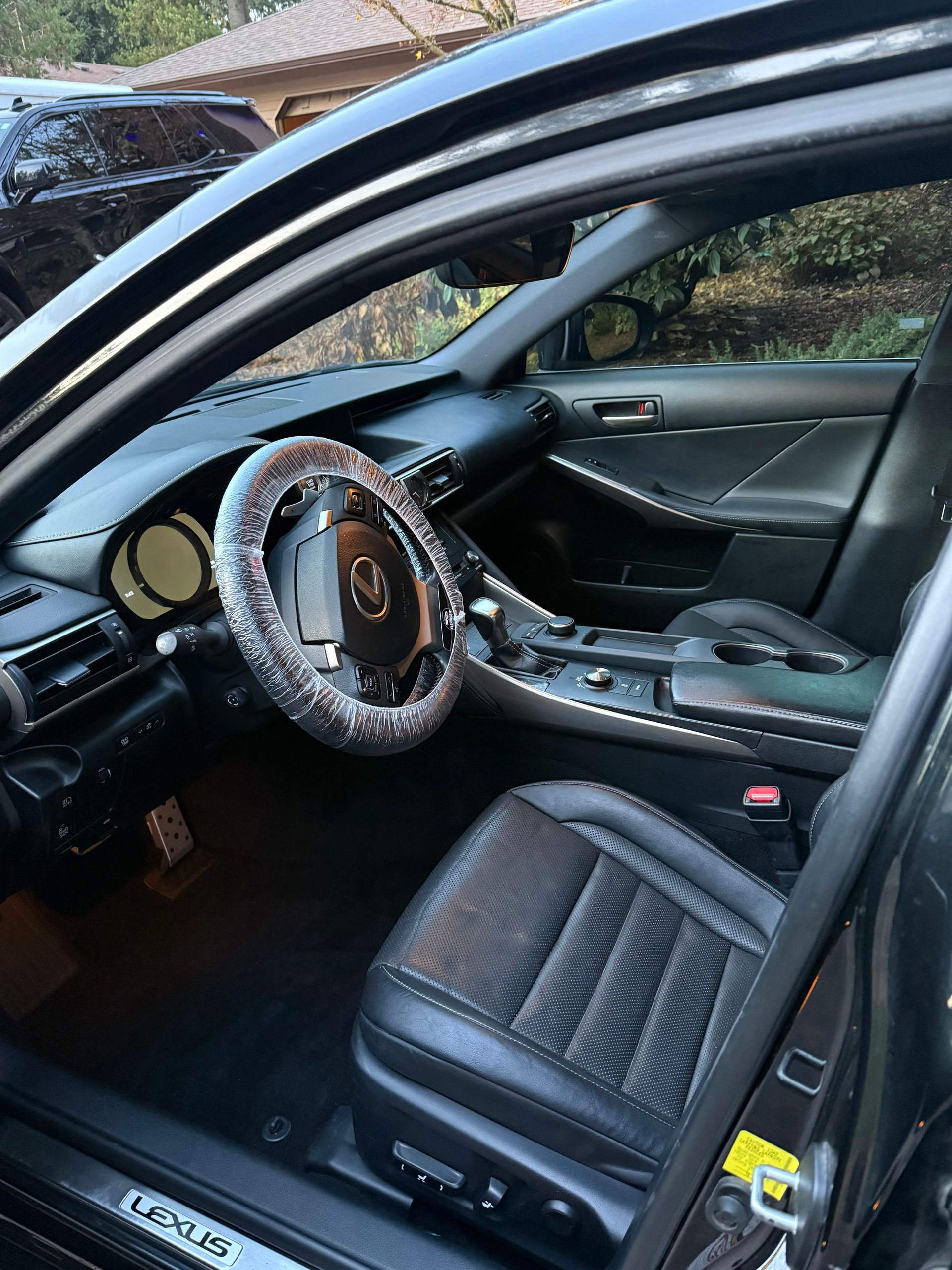 Car interior with a wood-trimmed steering wheel and black leather seats, viewed from the open driver’s door