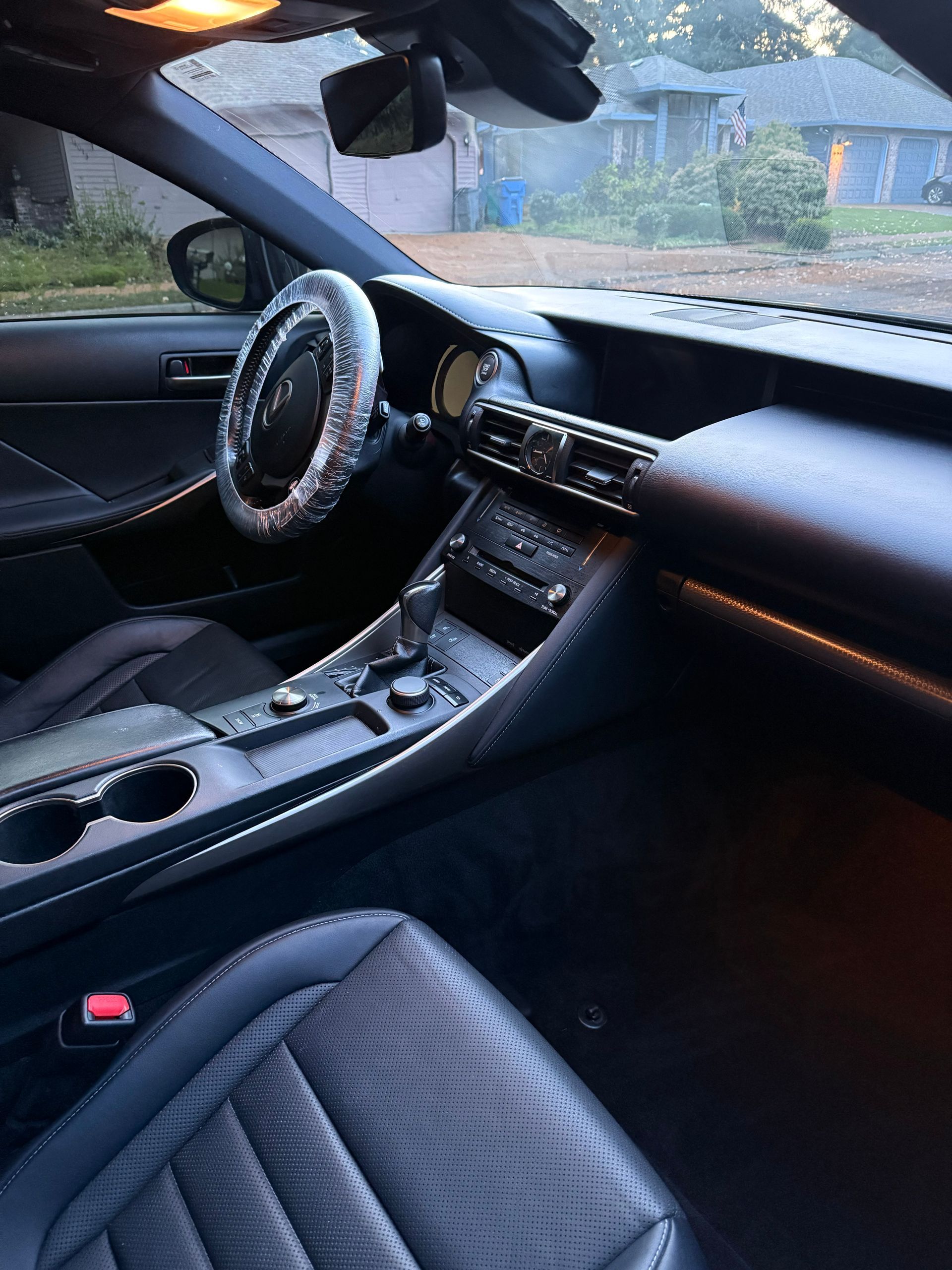 Car interior with black leather seats, steering wheel cover, and dashboard in a parked car at dusk