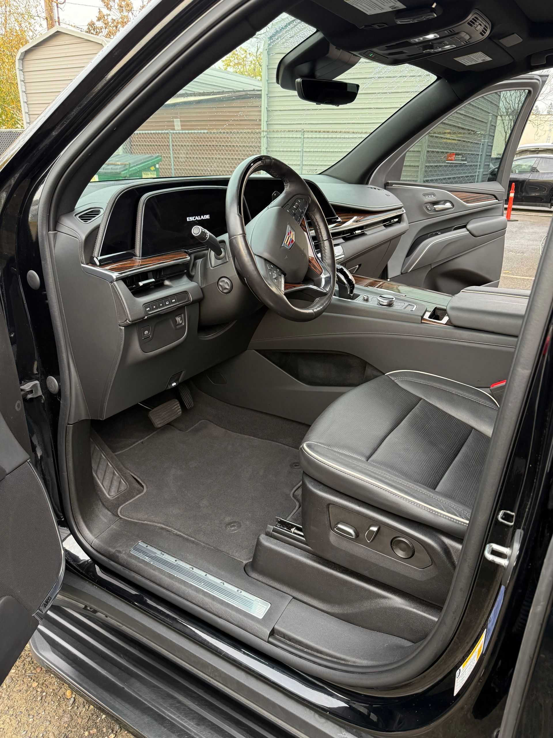 Car’s driver door open, showing black leather interior with steering wheel and dashboard.