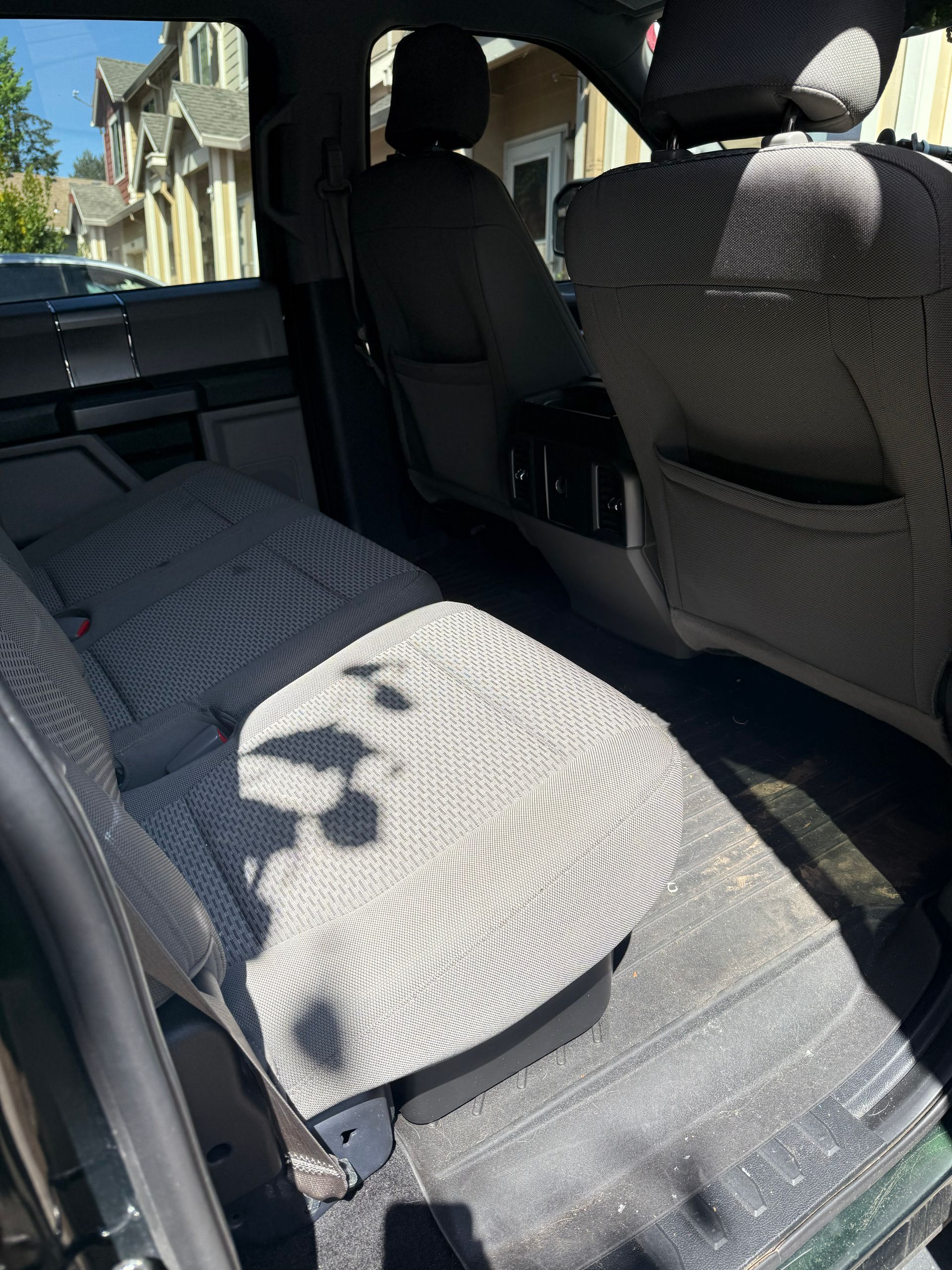 Car interior with rear seats folded flat, gray patterned seat covers, and sunlight streaming in from the side.