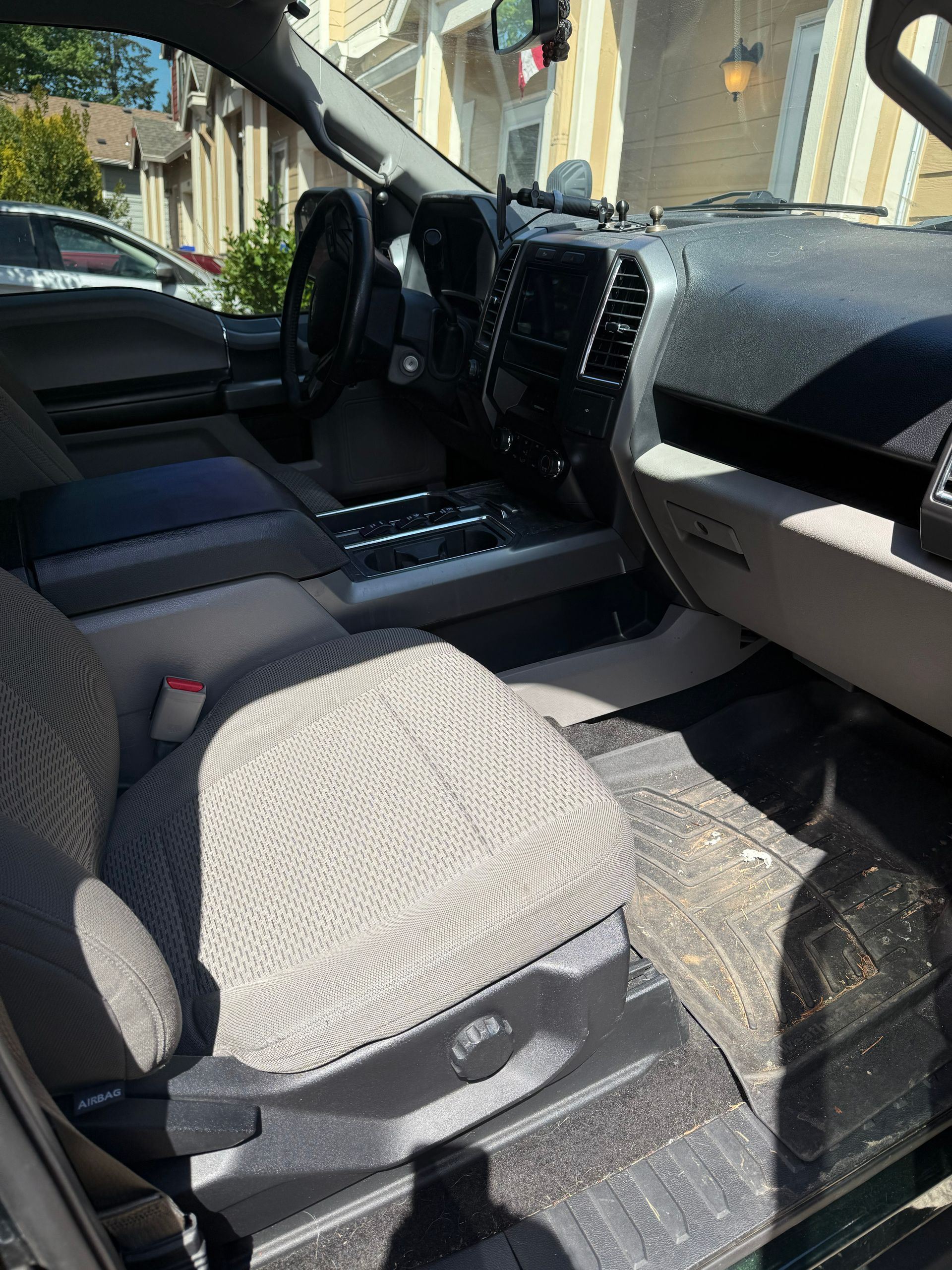 Car interior with gray fabric front seats and dashboard, parked in sunlight.