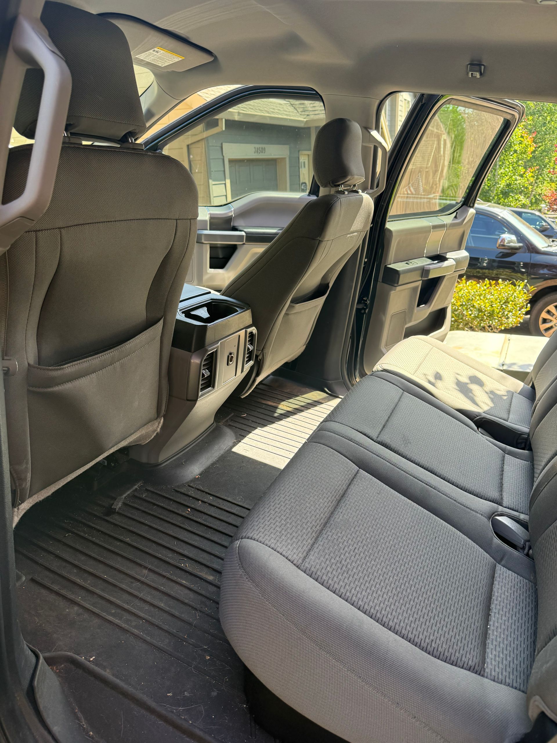 Interior of a car with gray seats and open door, showing the back seat and center console