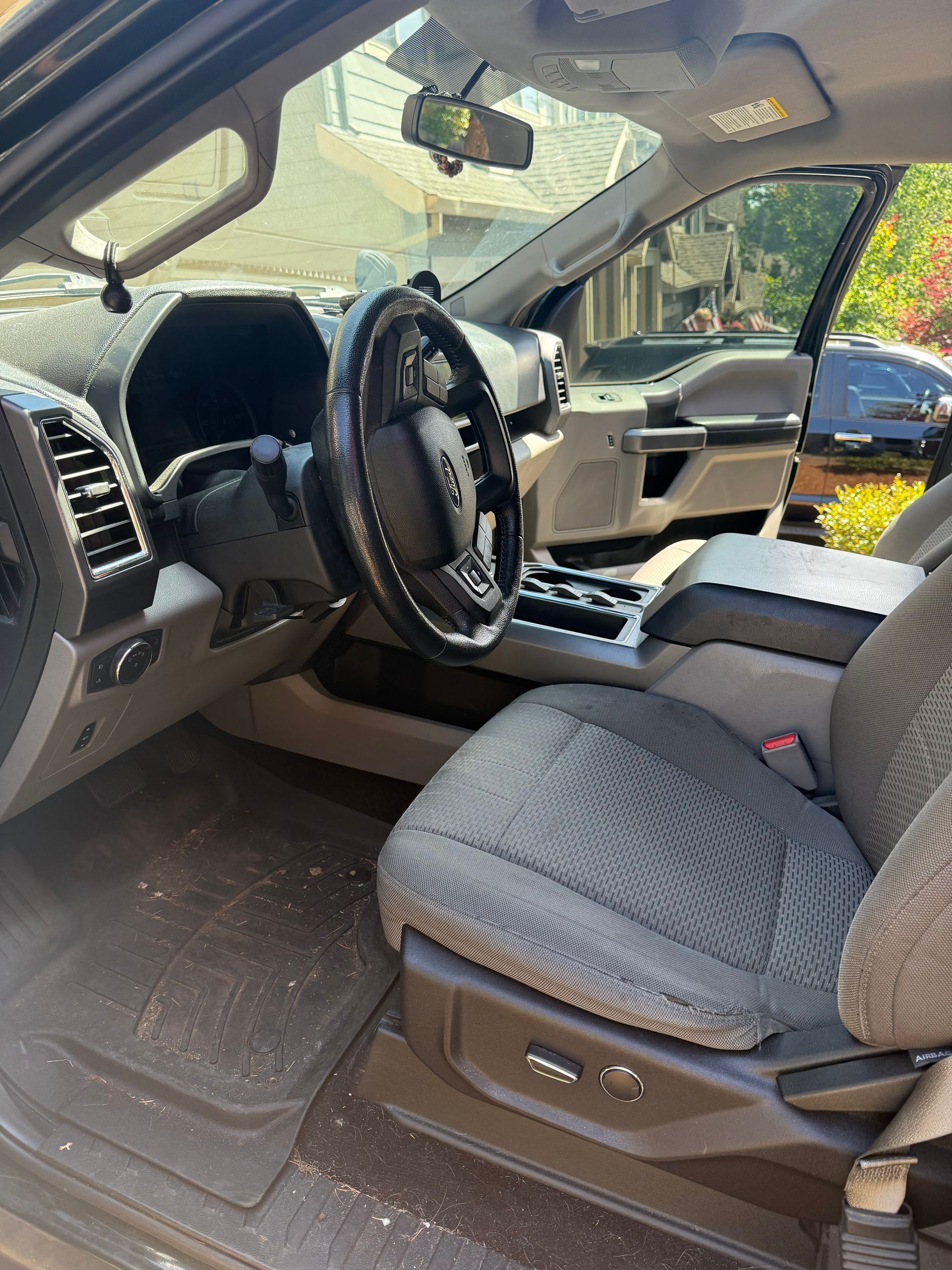 Open car door showing a beige interior with patterned seat covers and steering wheel dashboard.
