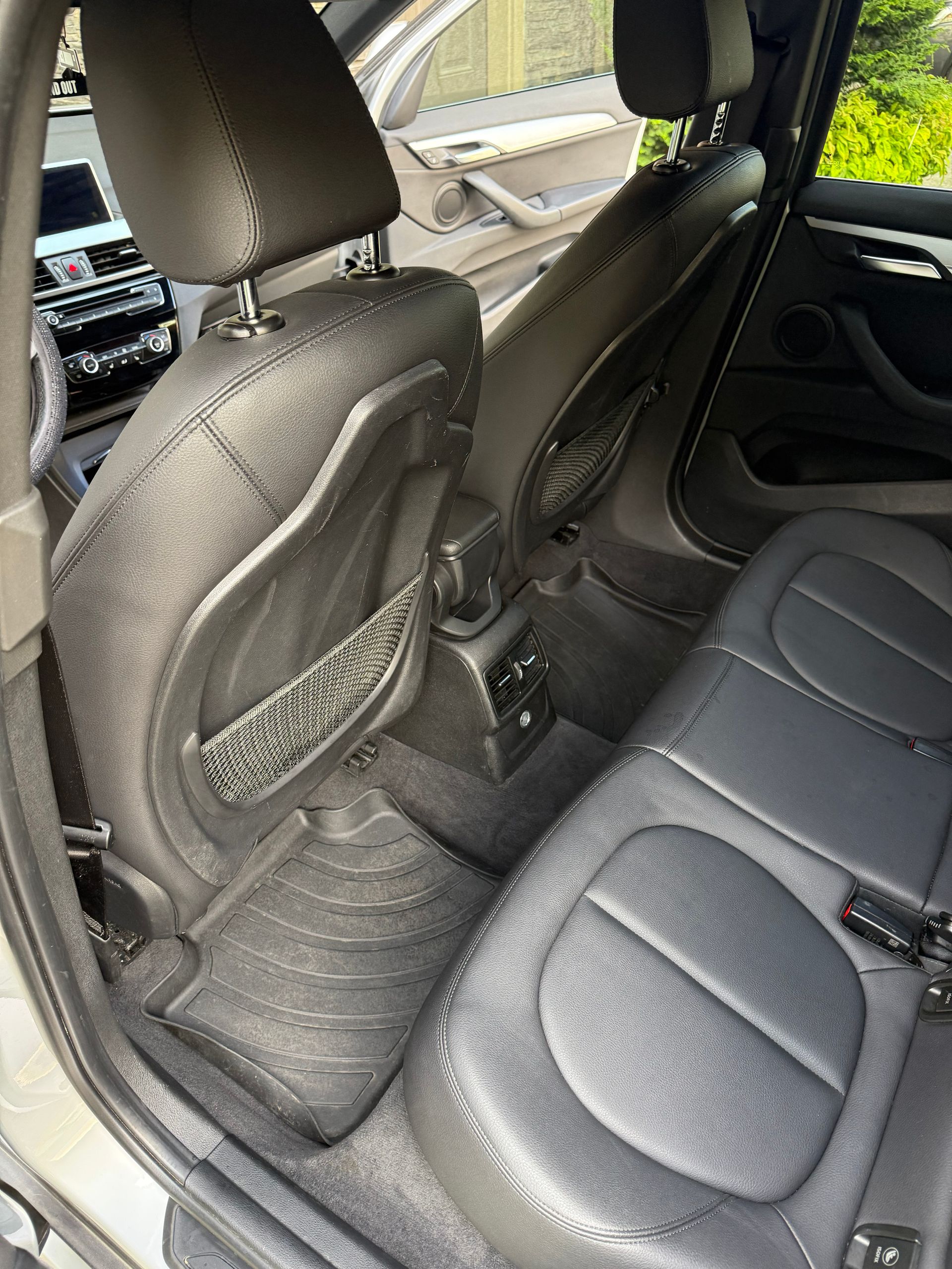 Car back seat with black leather seats and a folded front seat, showing the rear legroom area.