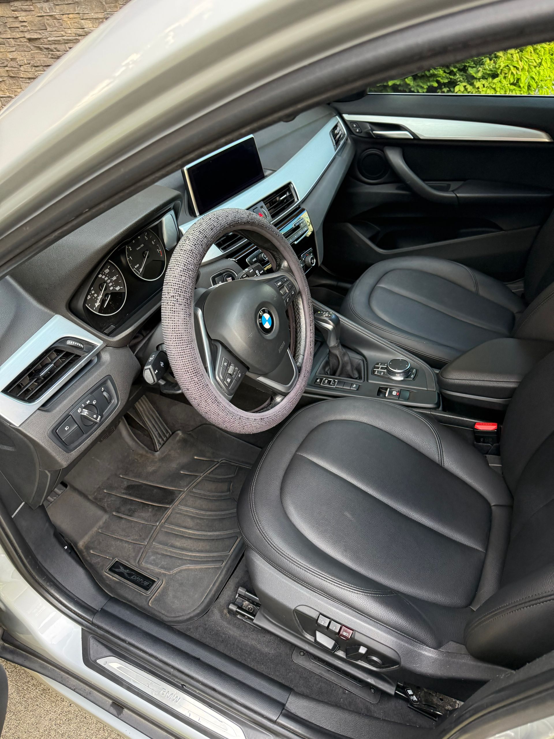 BMW interior with black leather seats, steering wheel cover, and center console, viewed from the open driver’s door