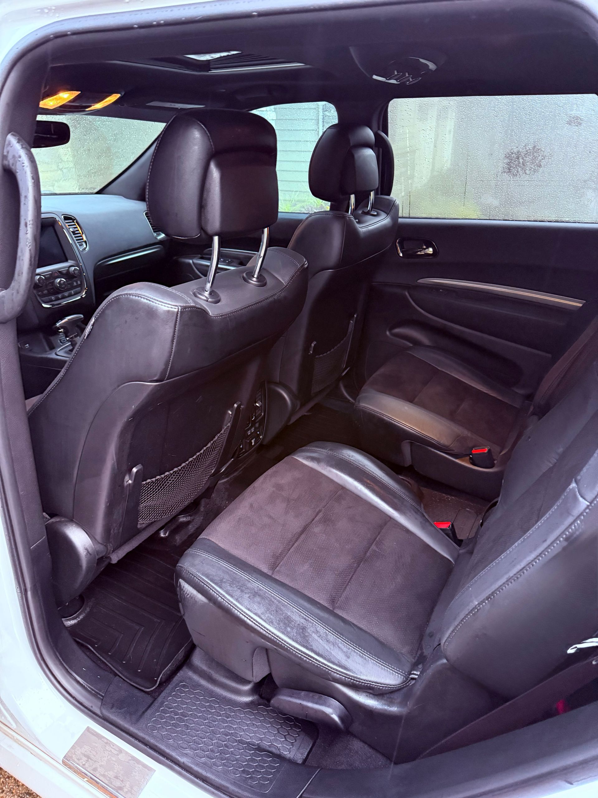 Backseat of a black car with dark upholstery and rain-speckled windows.
