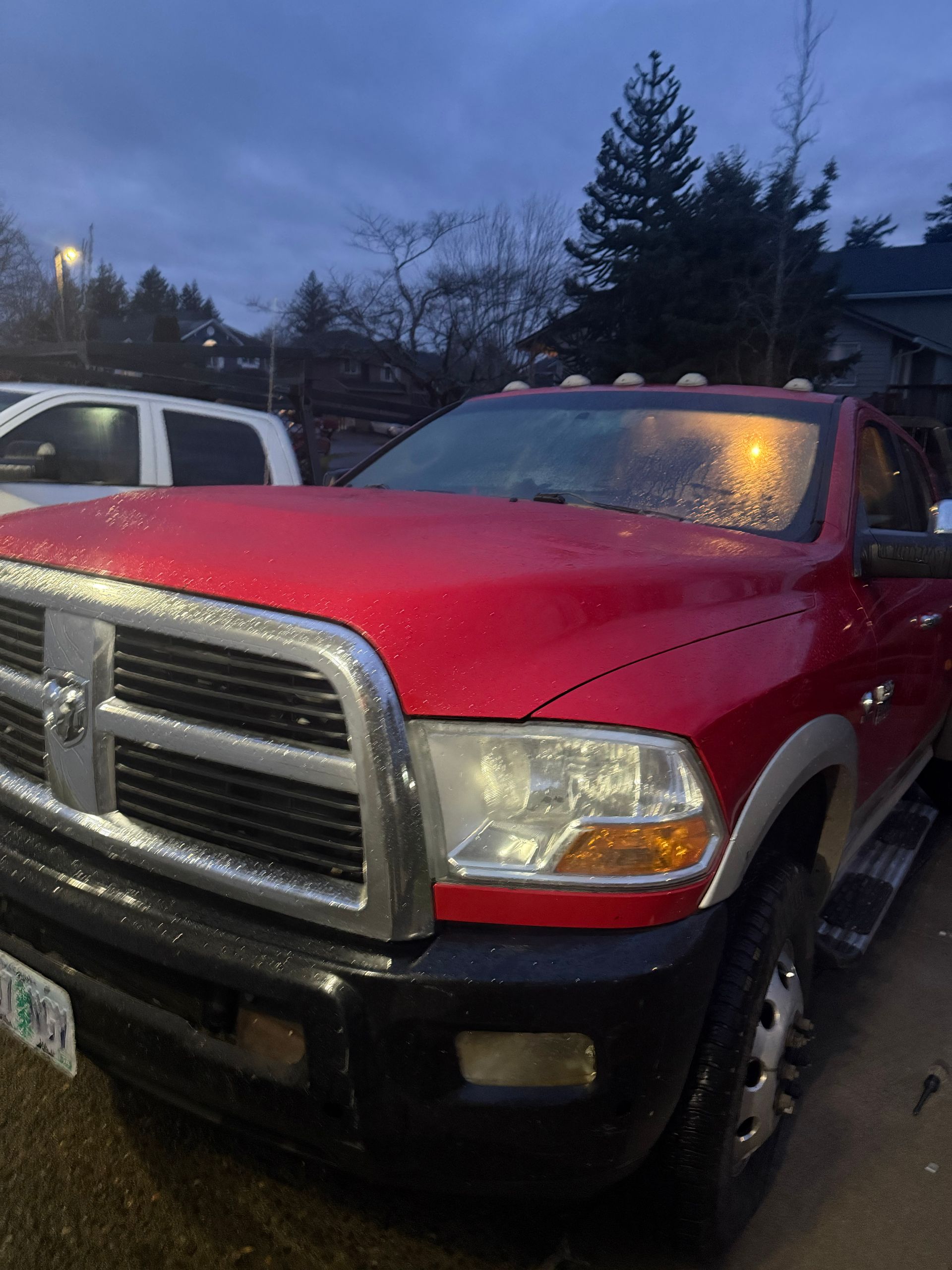 Red pickup truck parked at dusk with rain on the windshield and a white vehicle beside it.