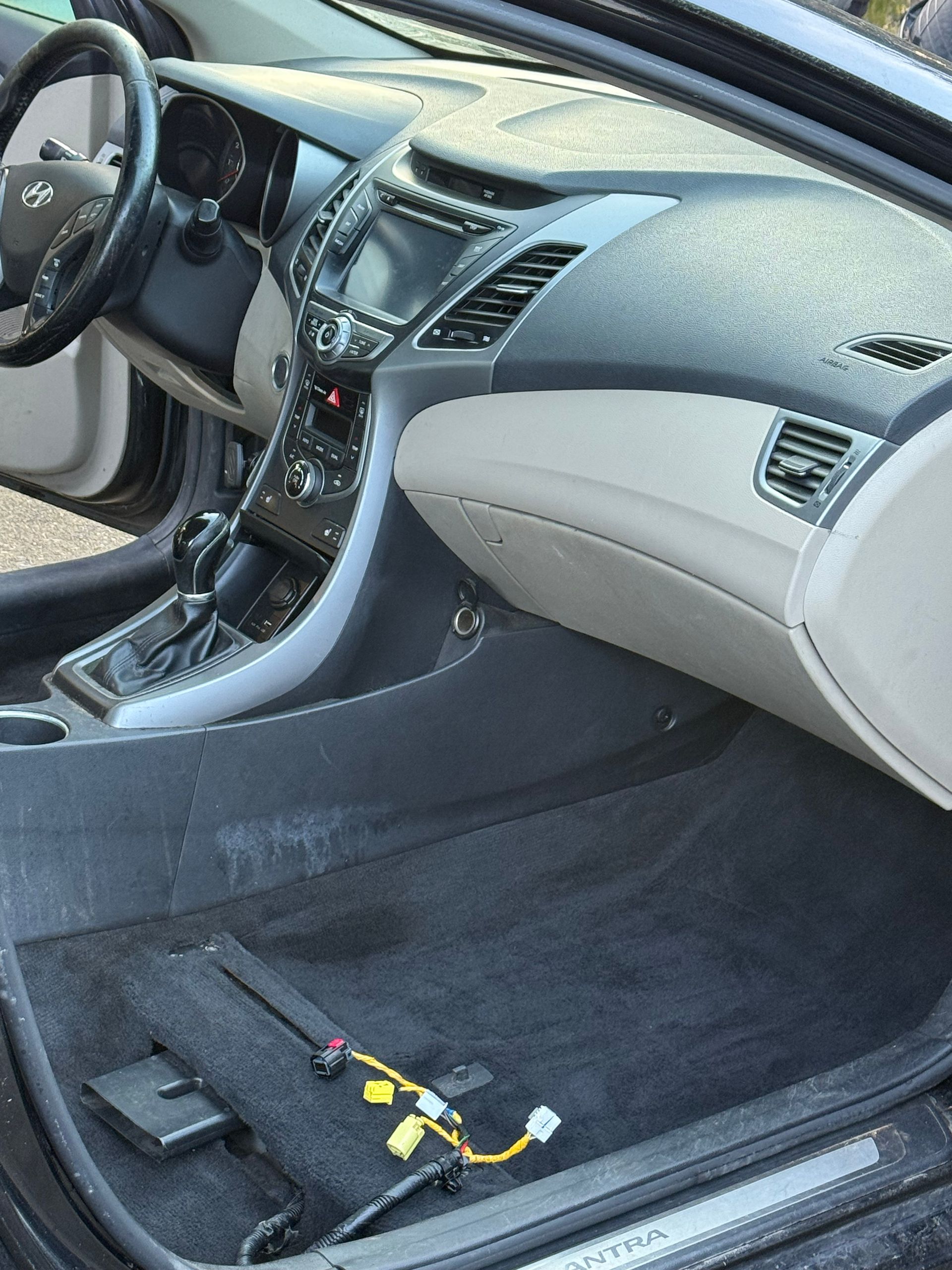 Car interior with passenger seat removed, exposing the floor and wiring near the center console.