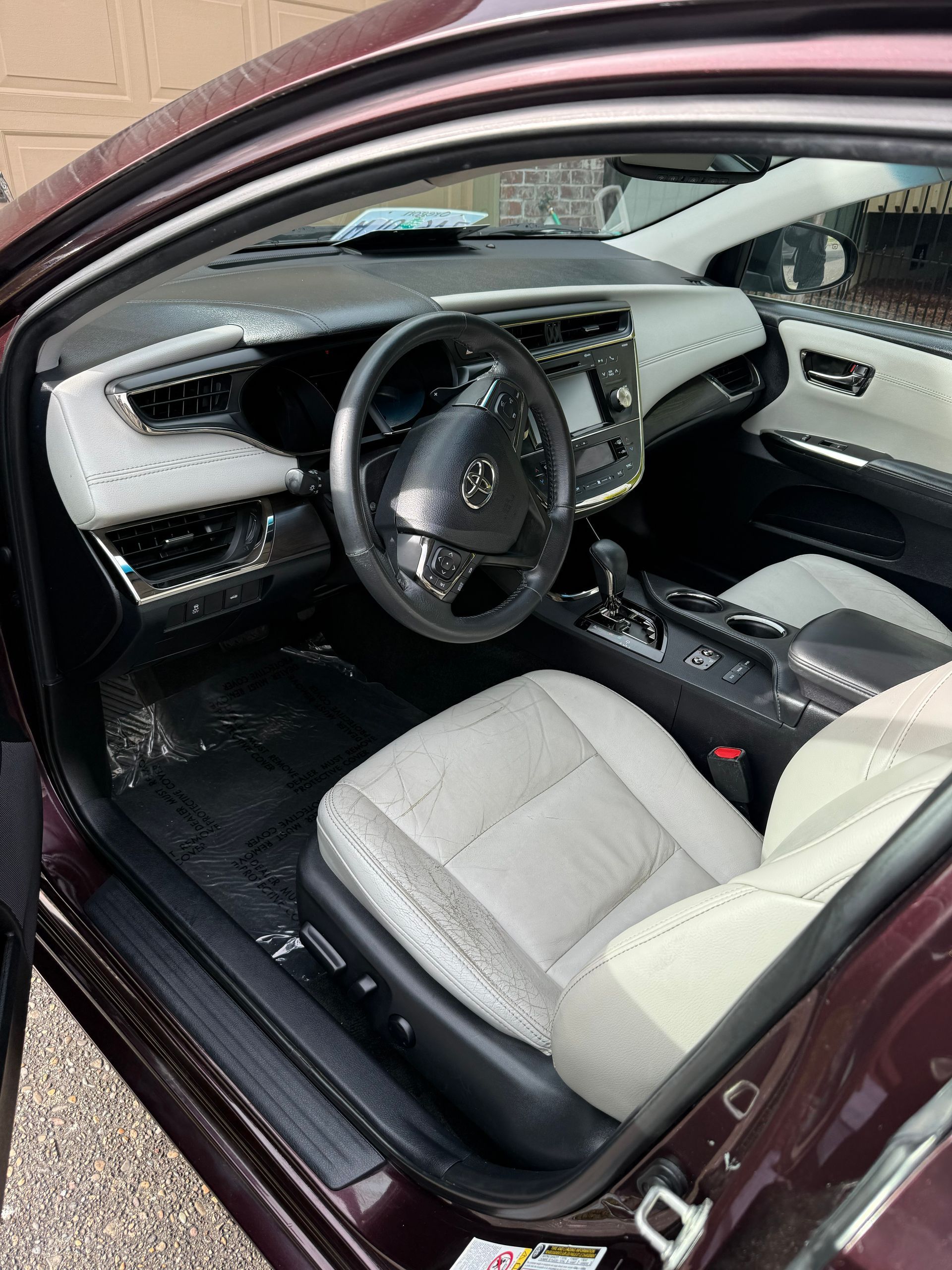 Luxury car interior with open door, black-and-white dashboard, steering wheel, and light leather seats