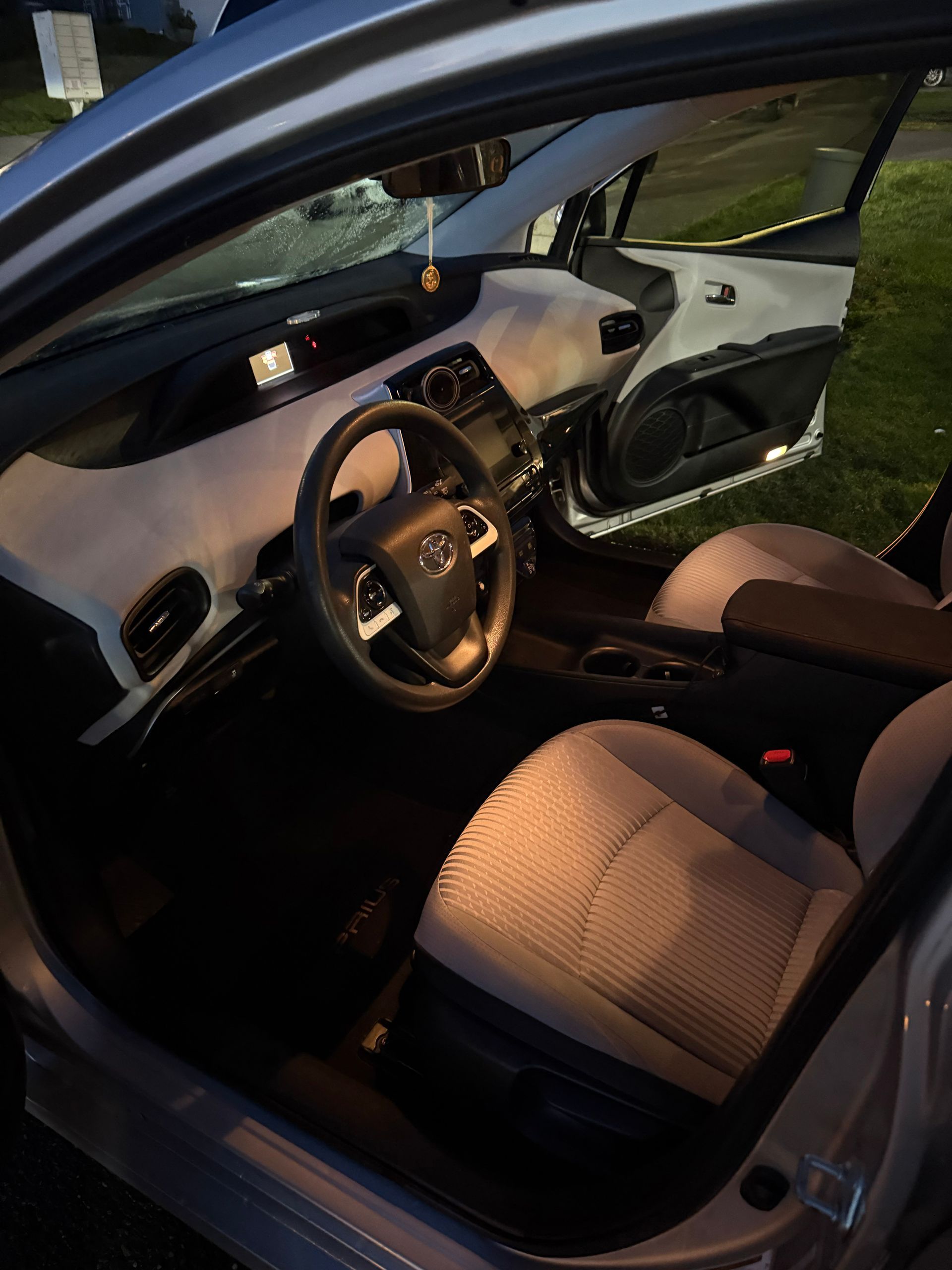 Car interior with open driver’s door, black steering wheel, and tan front seat at dusk