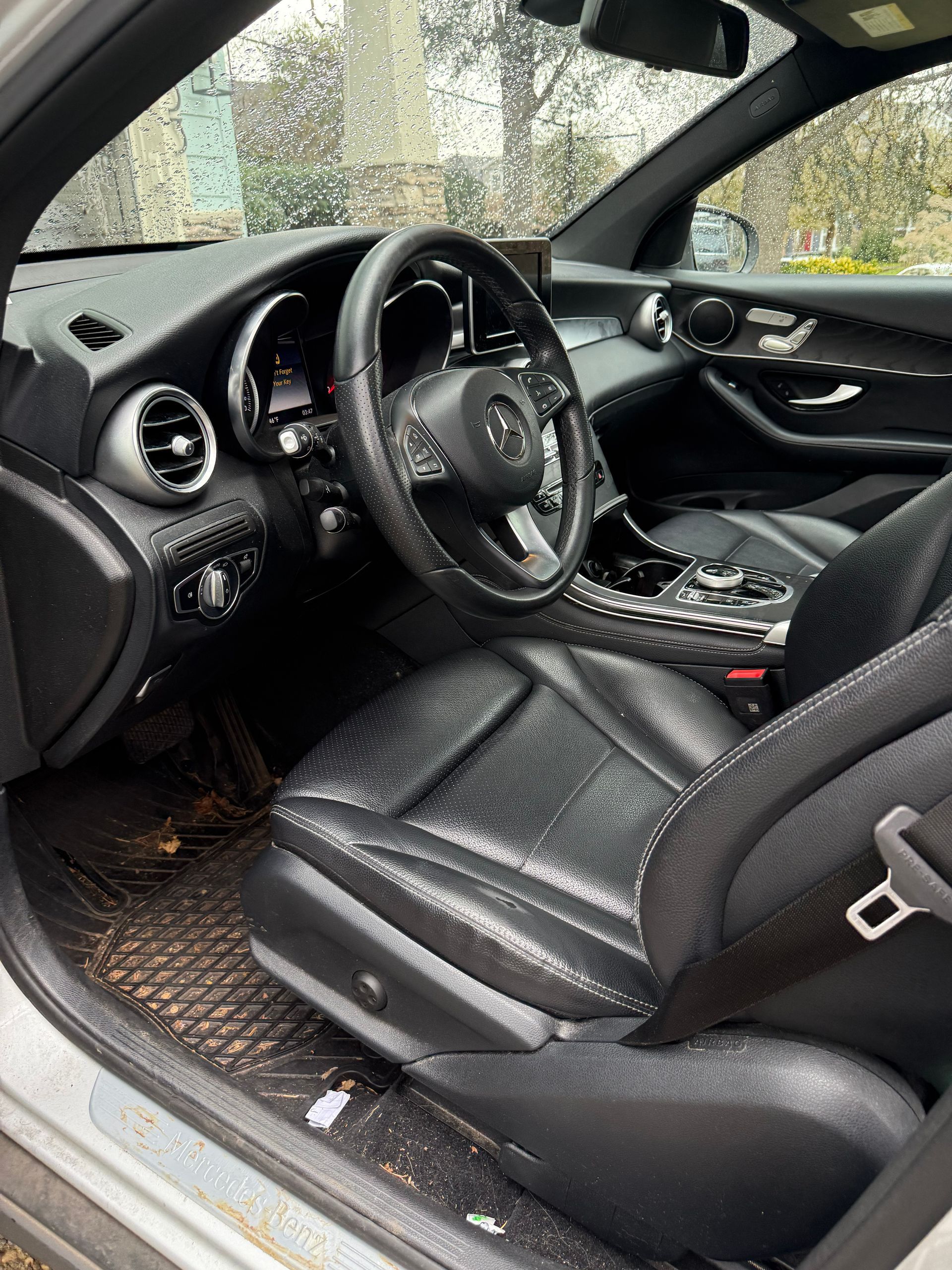 Black car interior with leather seats and steering wheel, viewed from the driver’s side window