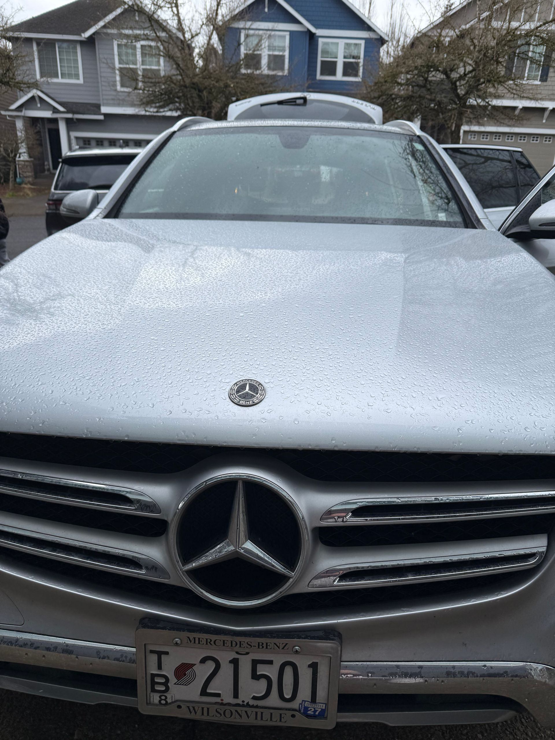 Silver Mercedes SUV front view with snow on hood, parked in a residential street