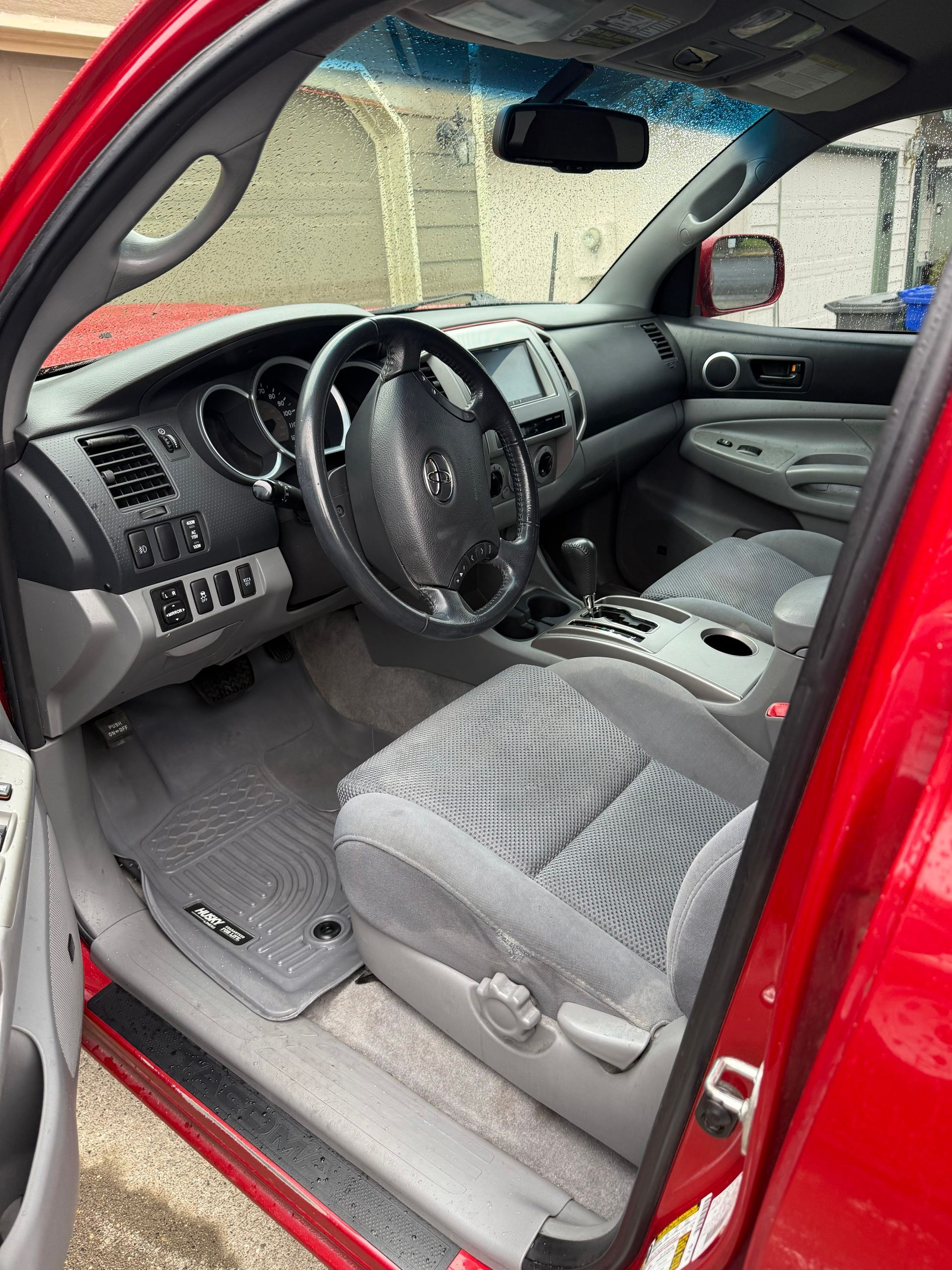 Red car interior with gray seats and dashboard, driver door open.