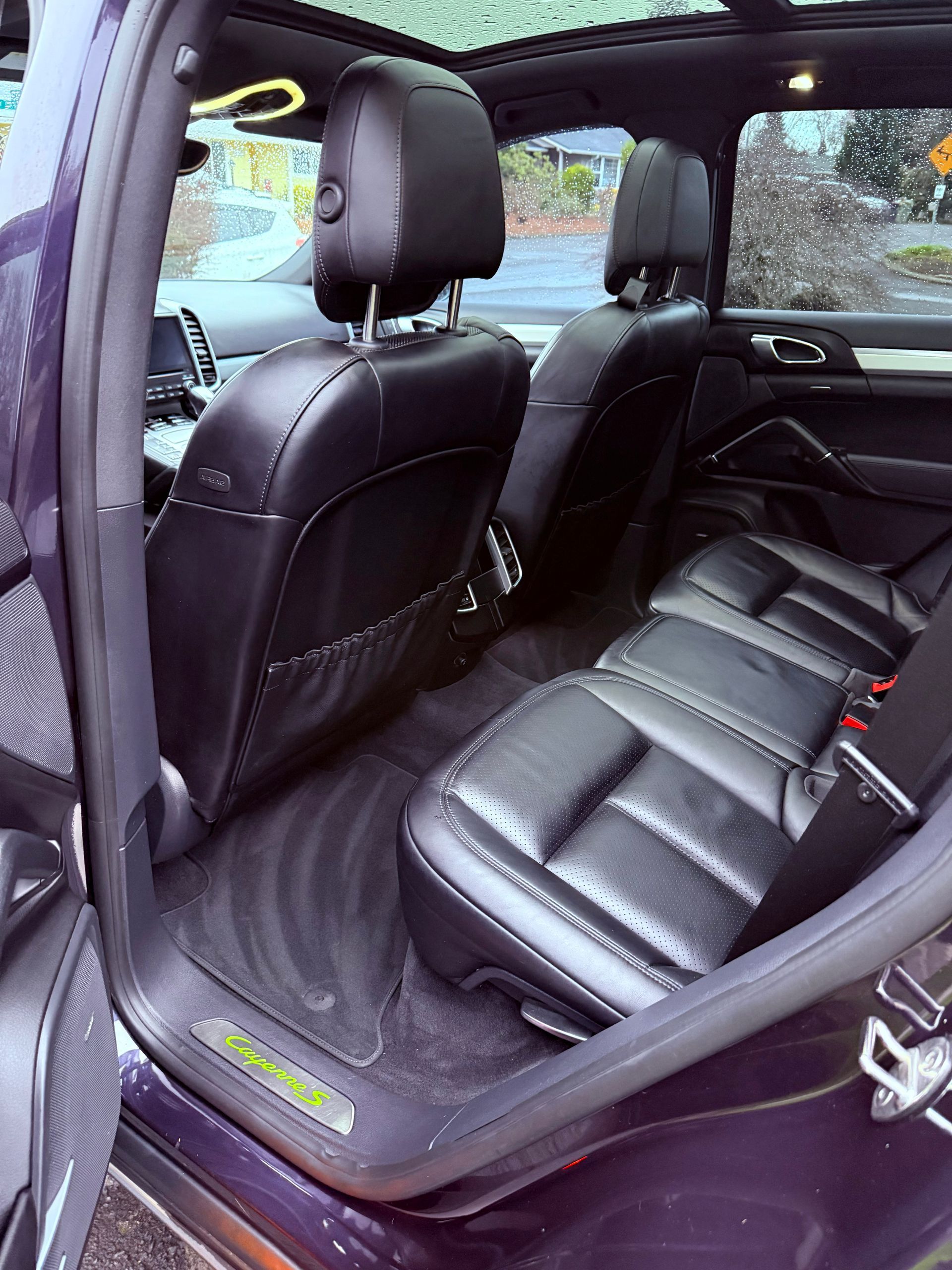 Backseat view of a black leather car interior with rain-speckled windows