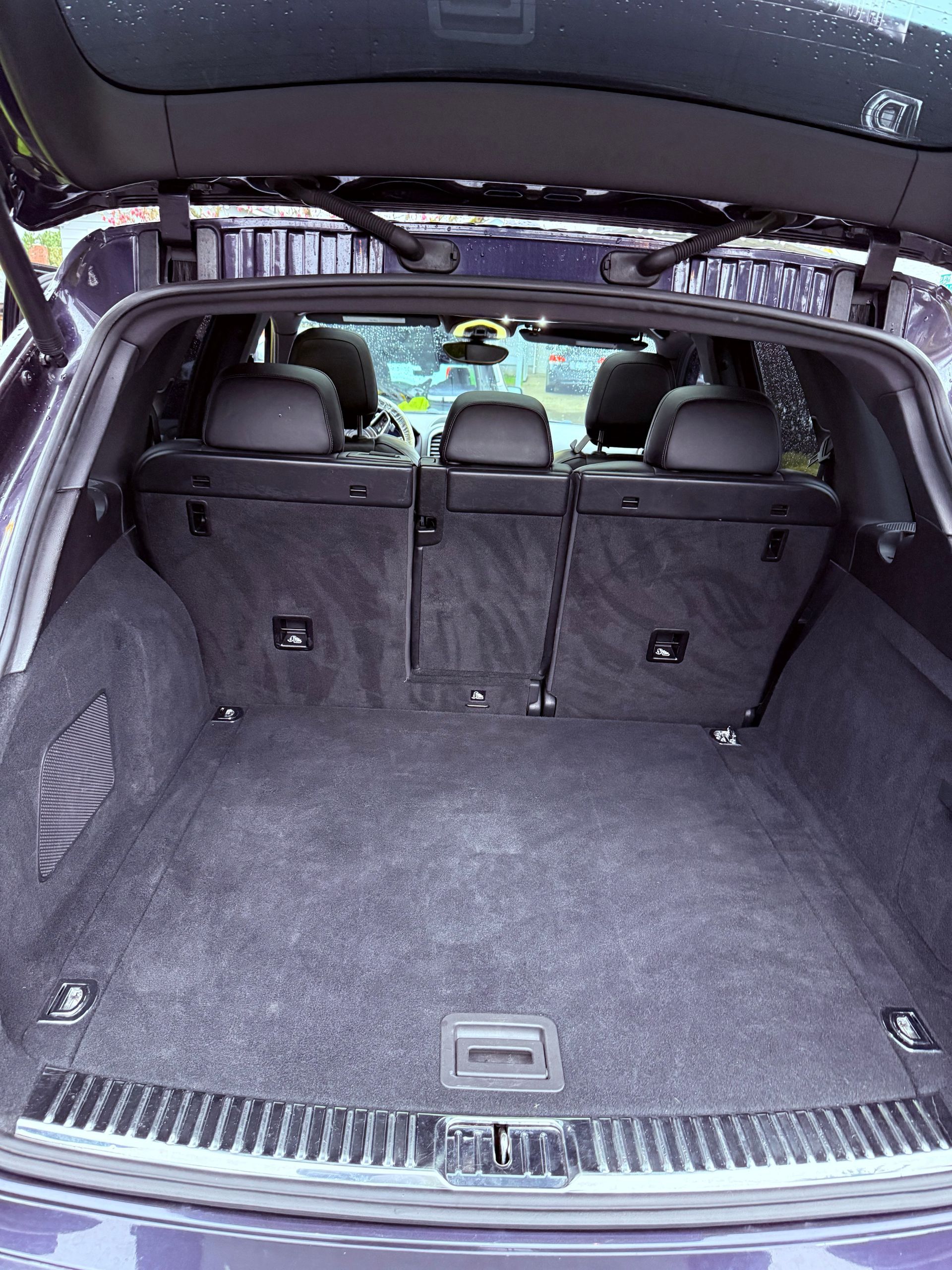 Empty car trunk with gray carpet and folded rear seats, viewed from the open hatchback.