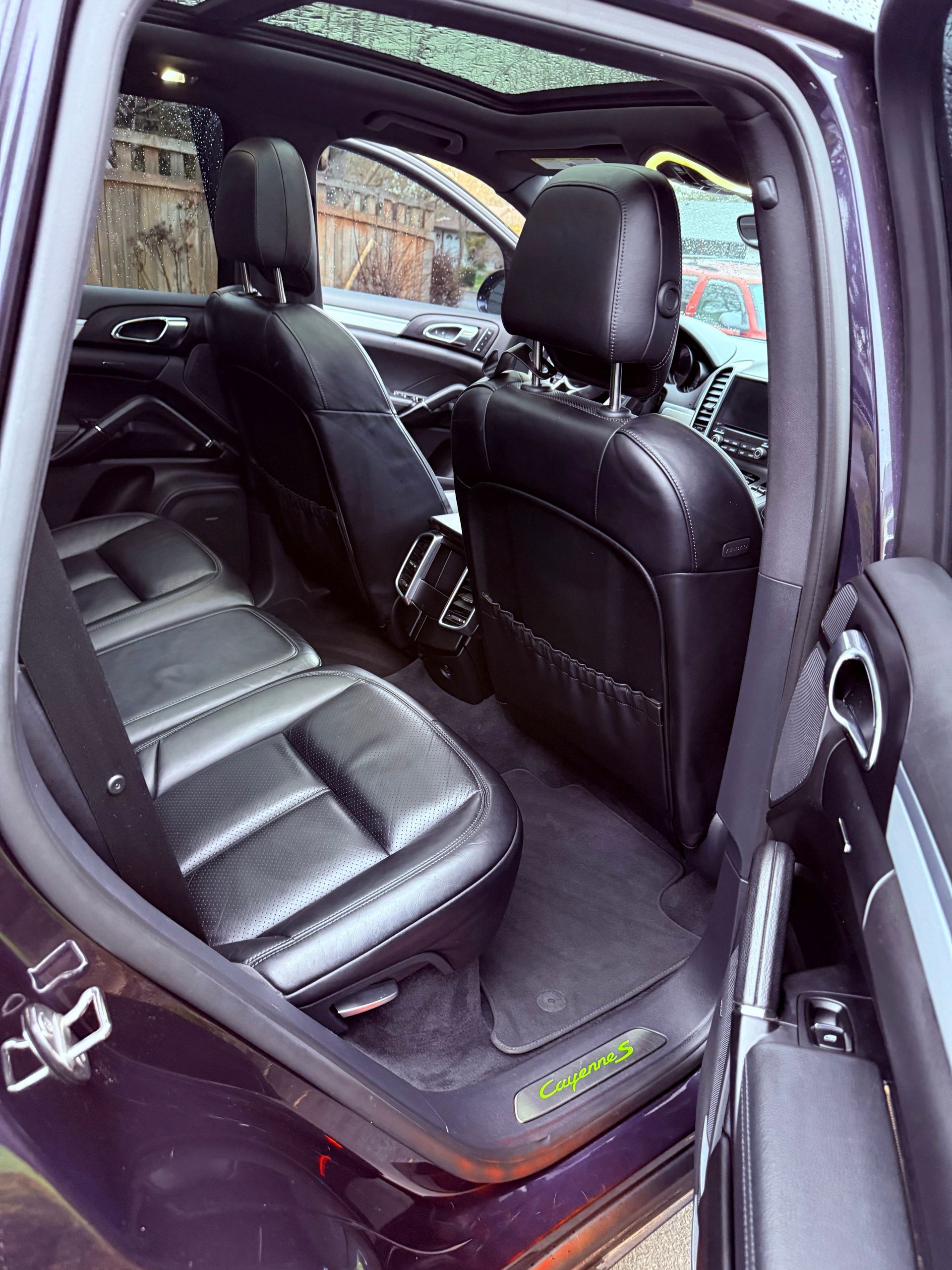 Open car rear door showing black leather back seat and interior, viewed from outside.