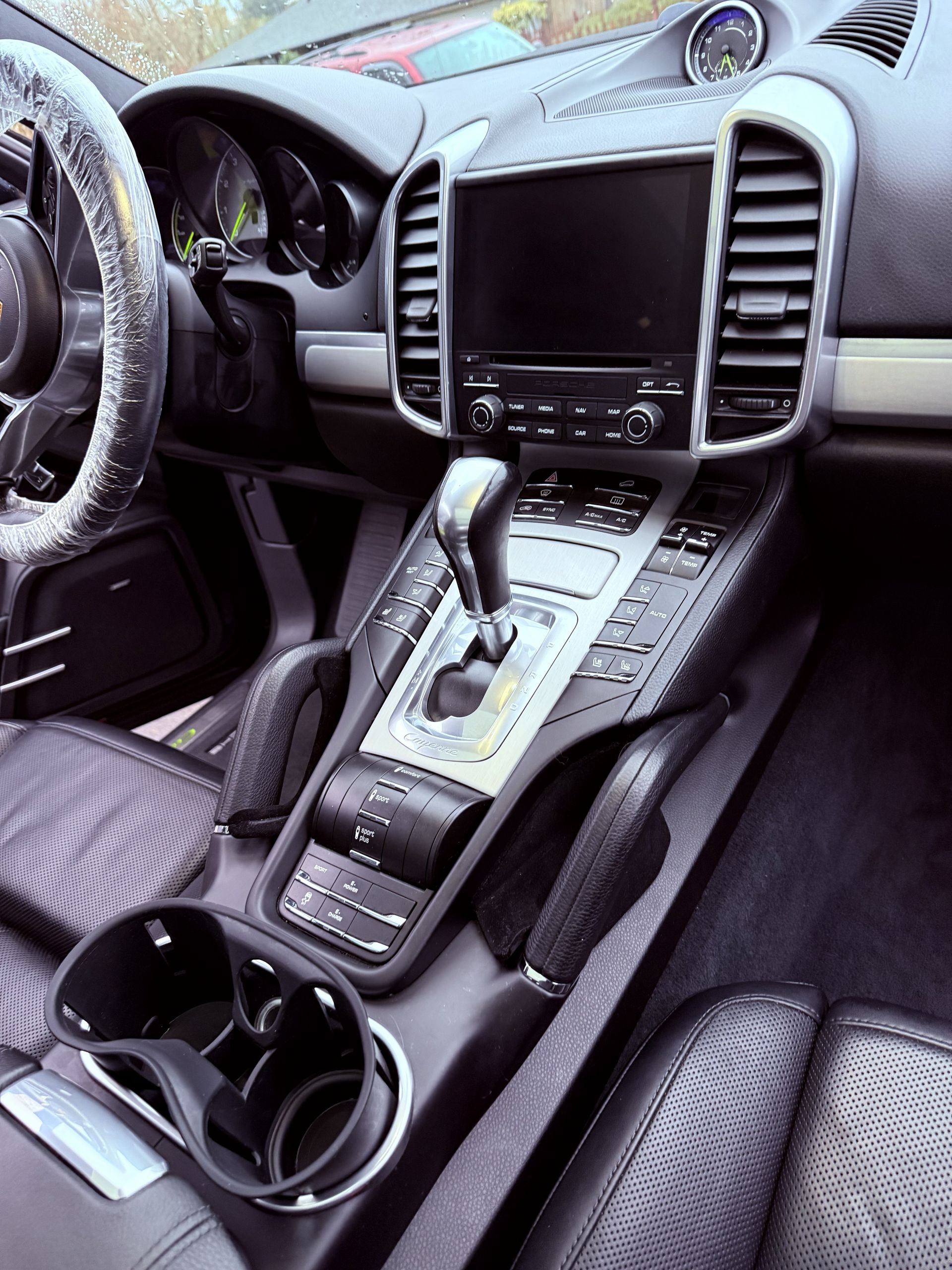 Car interior with a center console, gear shifter, touchscreen, and cup holders in black and silver.