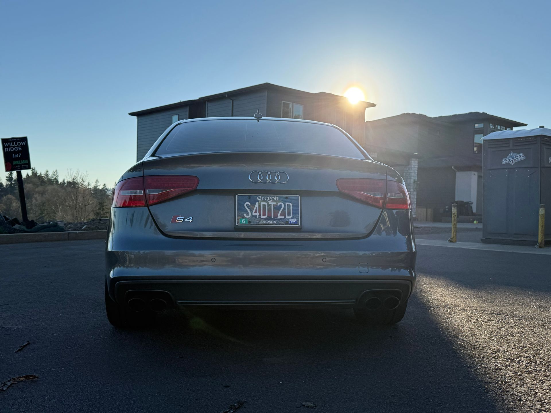 Rear view of a gray Hyundai sedan parked in a lot at sunrise, with sun glare behind it.