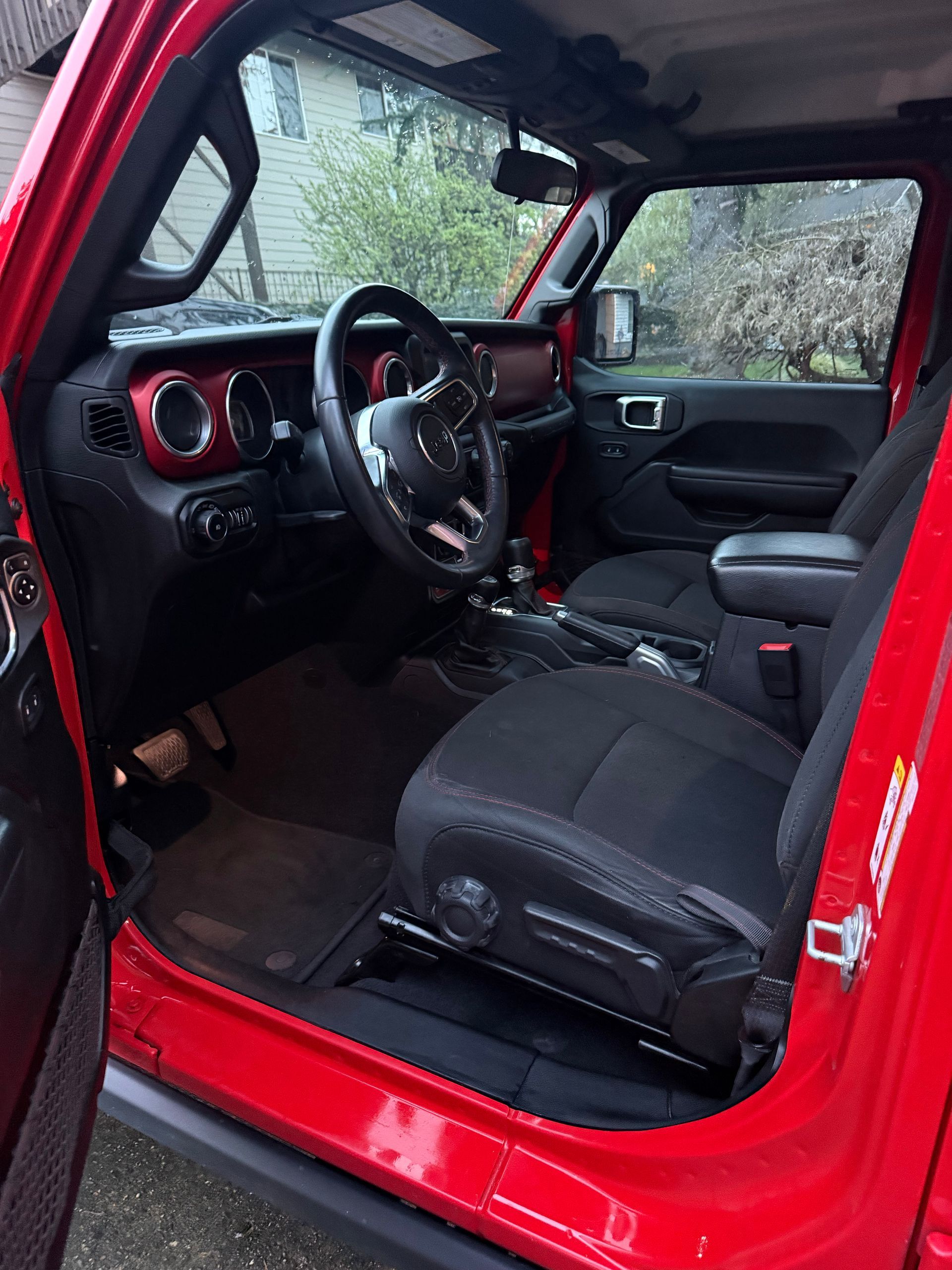 Red vehicle interior with black seats and dashboard, viewed through the open driver’s door.