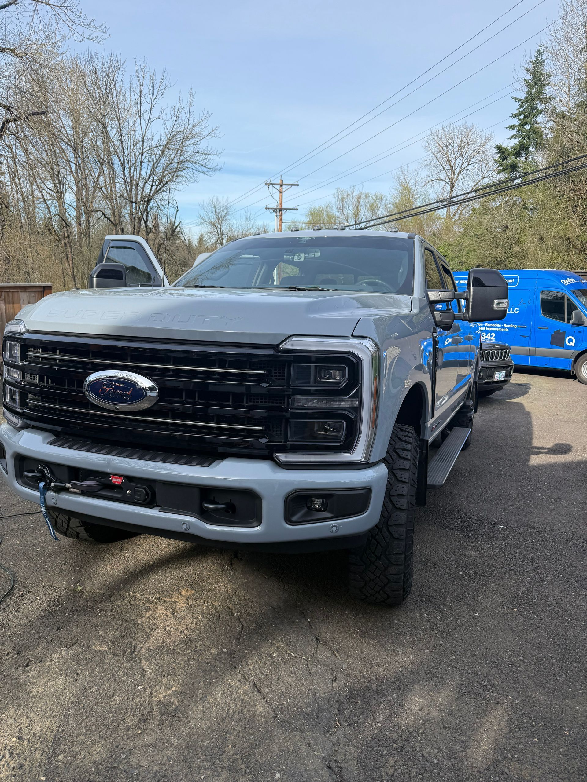 Silver Ford pickup truck parked outdoors beside a blue truck on a wooded lot