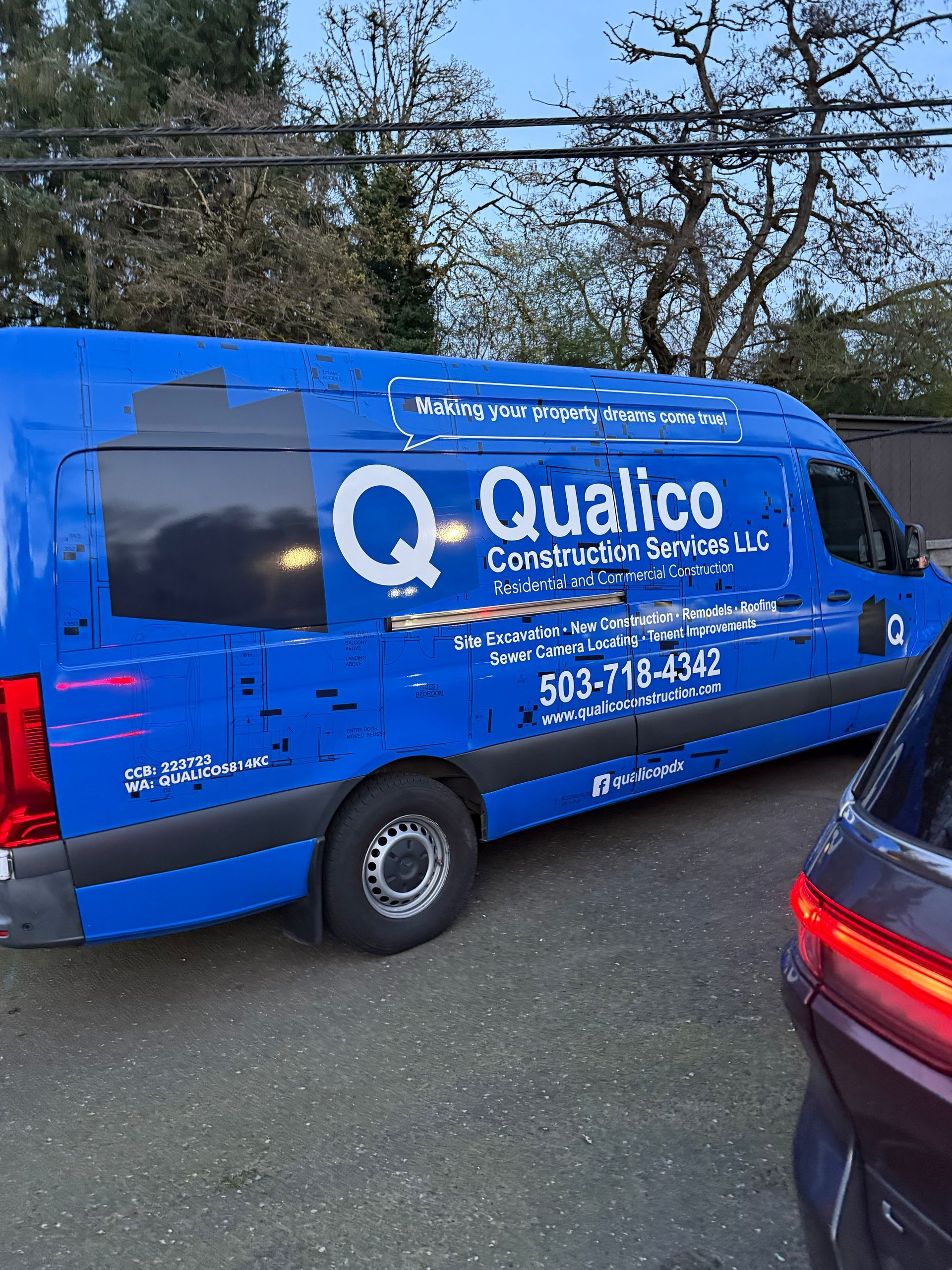 Blue Qualico Commercial Services van parked beside a dark car on a roadside.