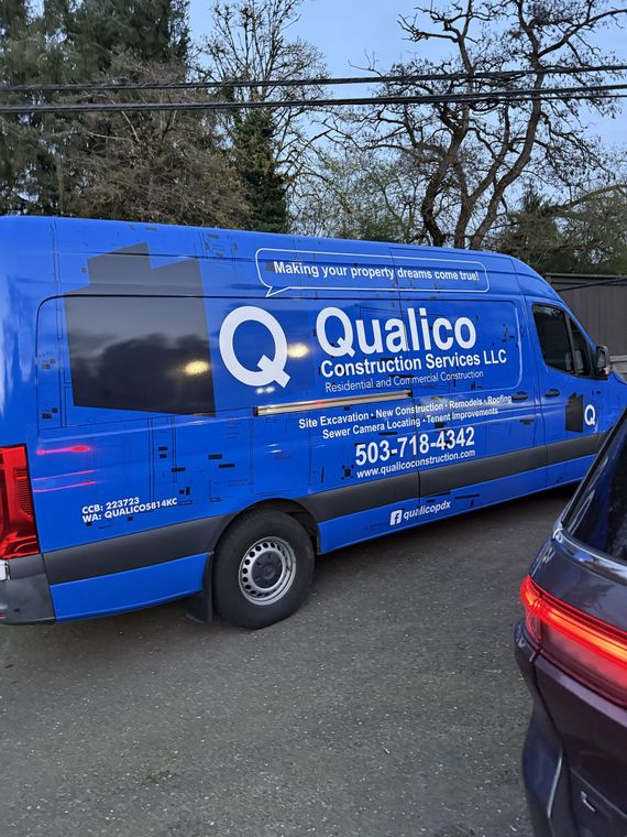 Blue Qualico Commercial Services van parked on a street beside a car and trees.