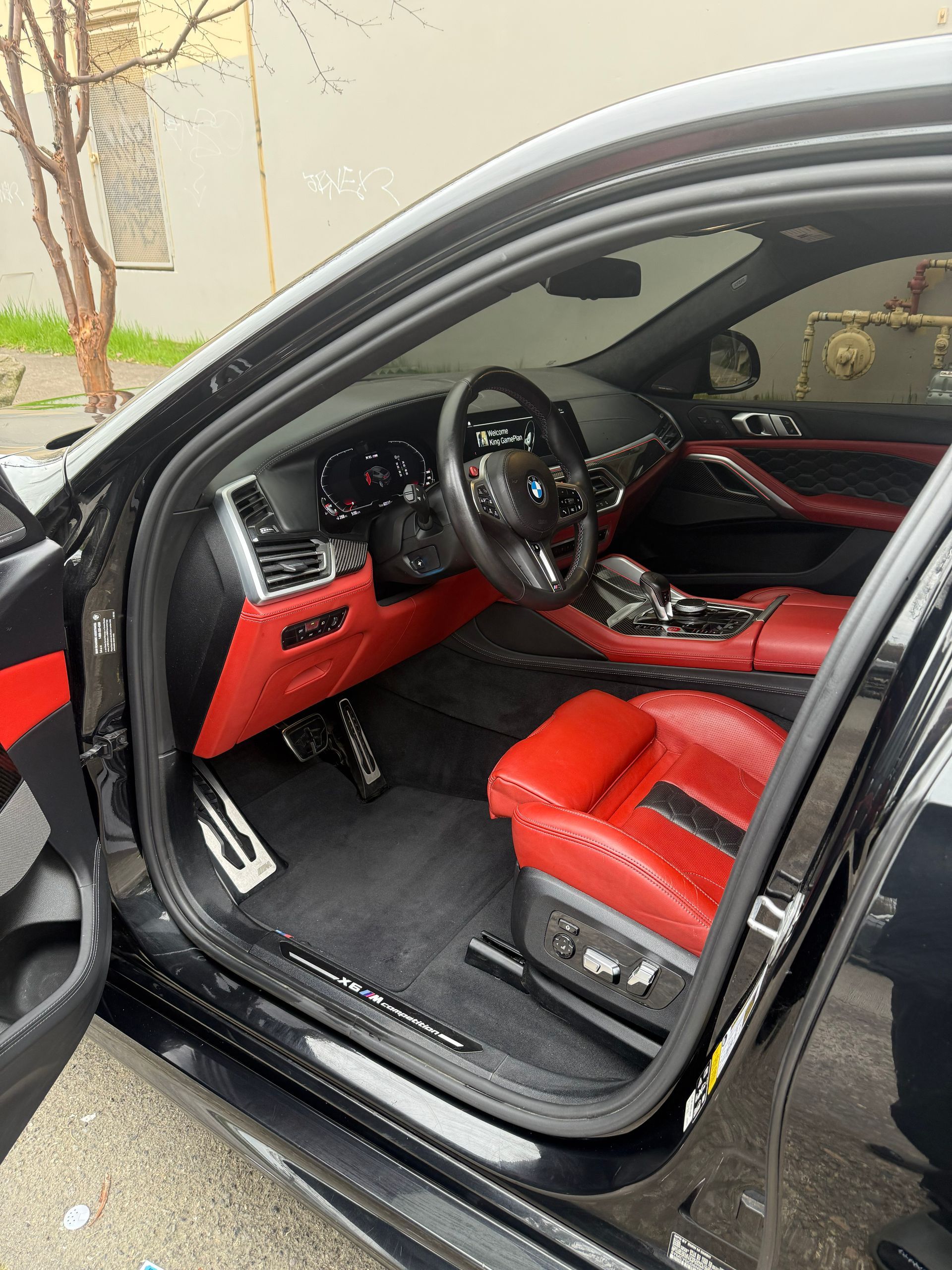 Open car door revealing a red-and-black luxury car interior with sporty seats and dashboard