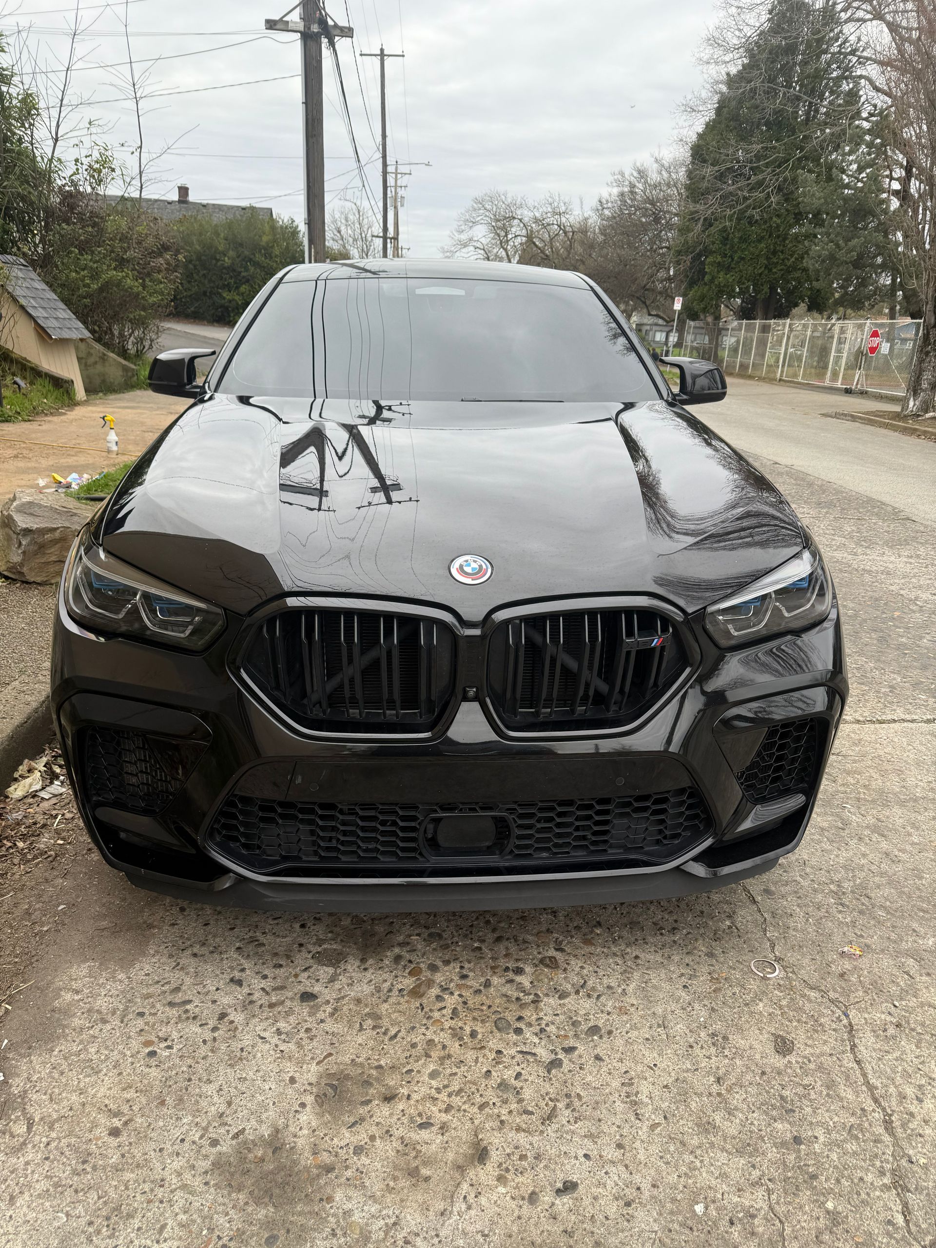 Black BMW sedan parked on a wet roadside under an overcast sky
