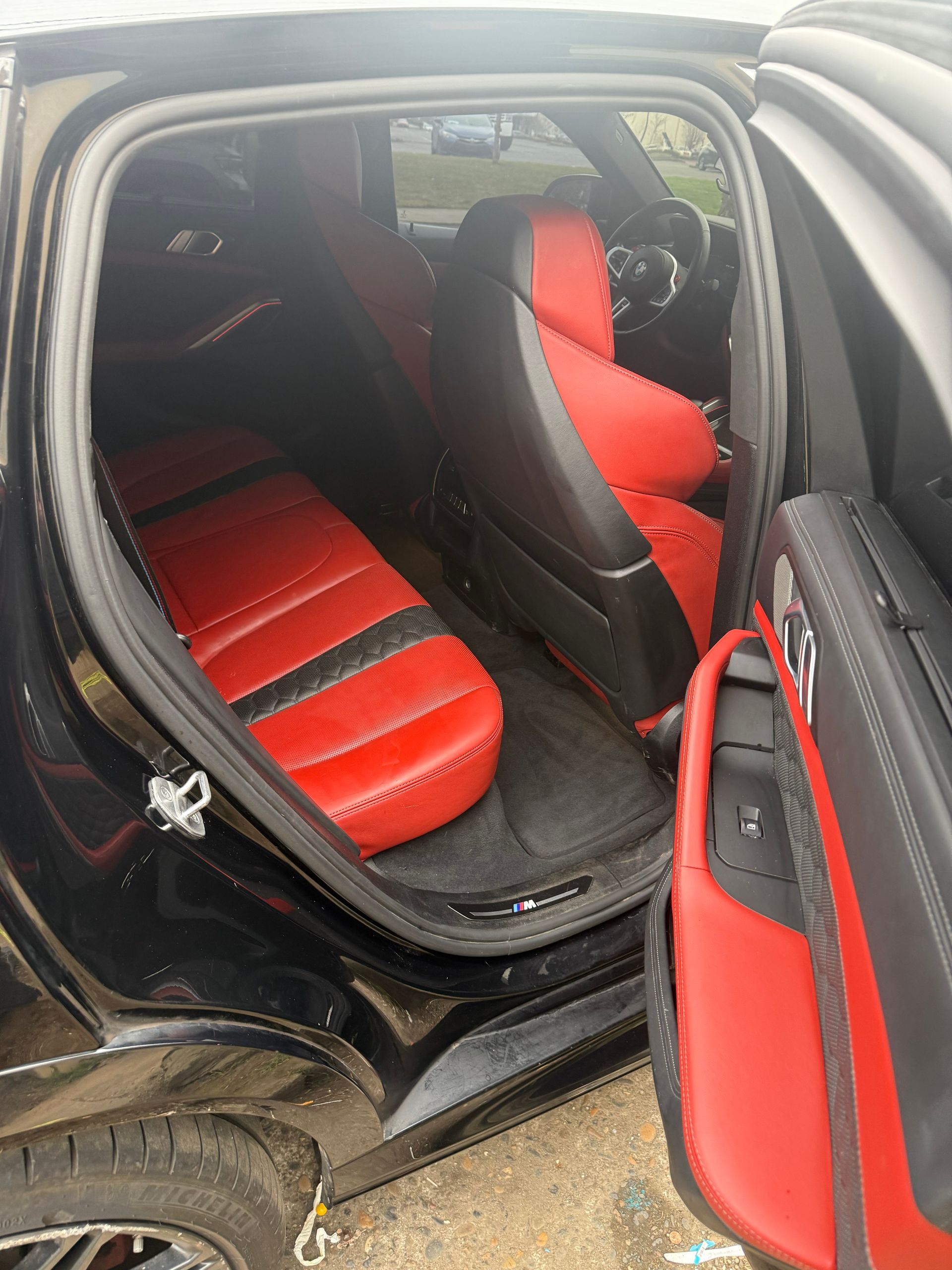 Black car with open doors showing red and black custom seat covers inside and on the front door panel