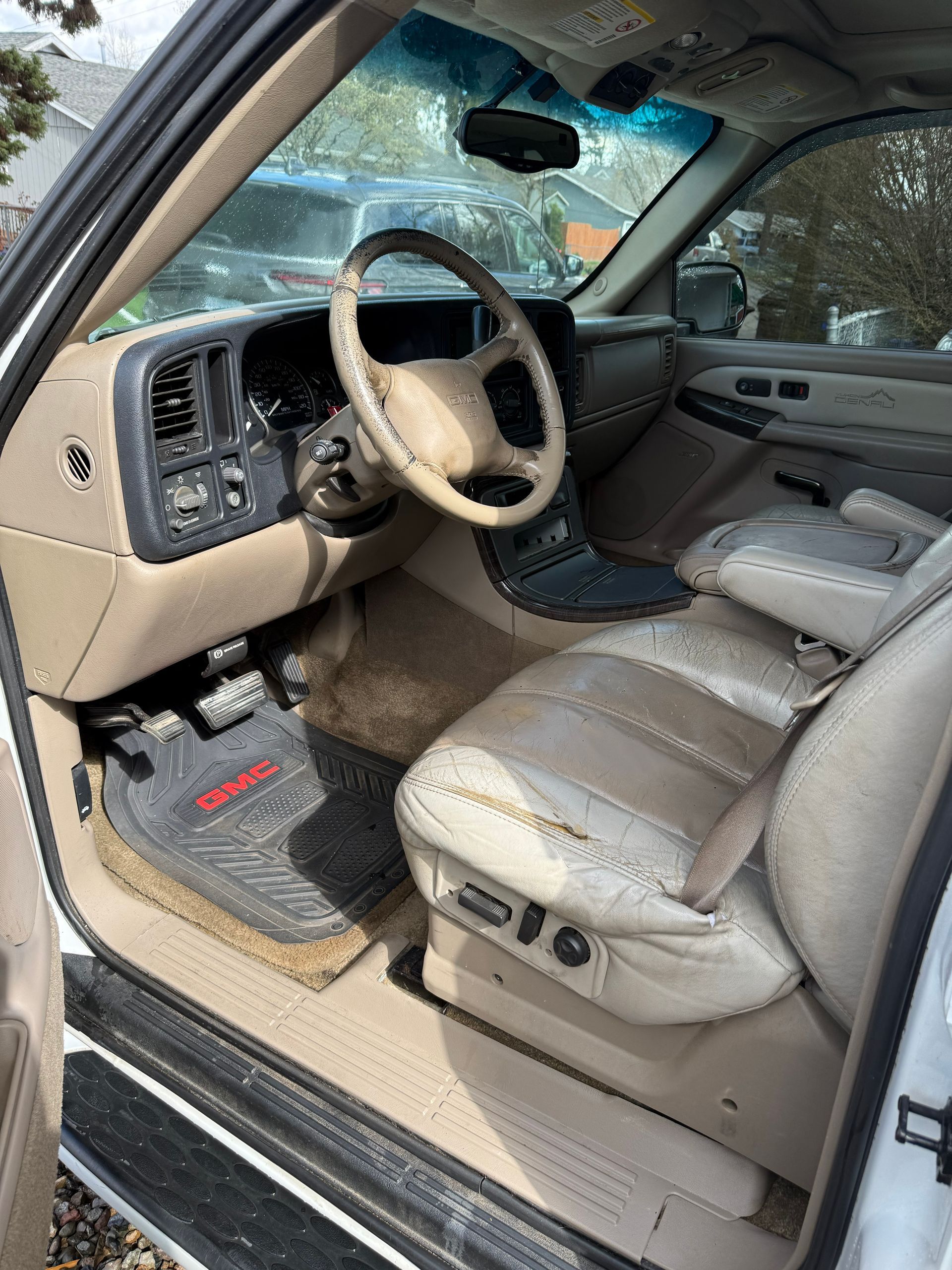 Open car door showing beige leather interior with windshield damage and deployed steering wheel airbag