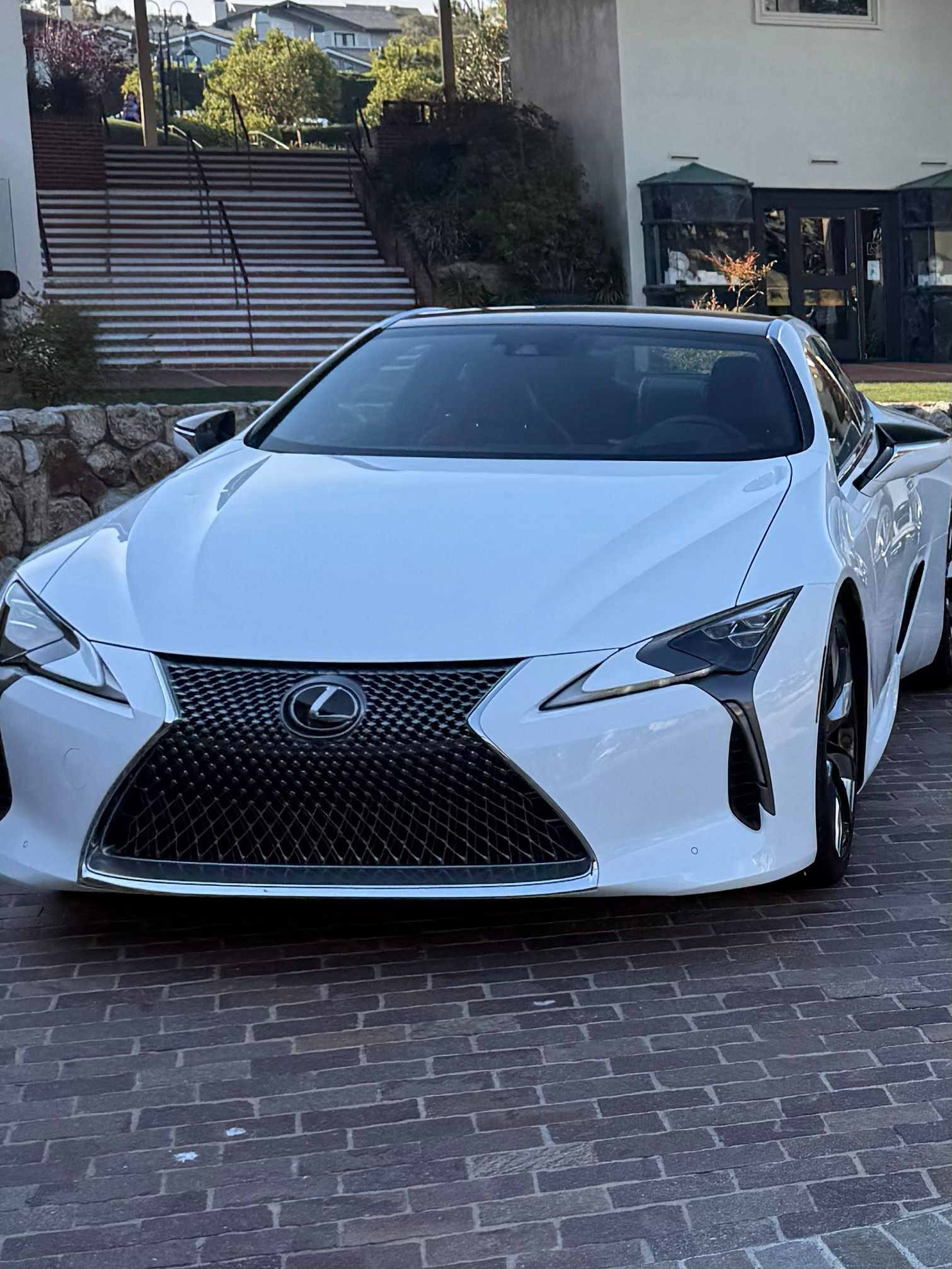 White Lexus coupe parked on a brick driveway in front of steps and a house
