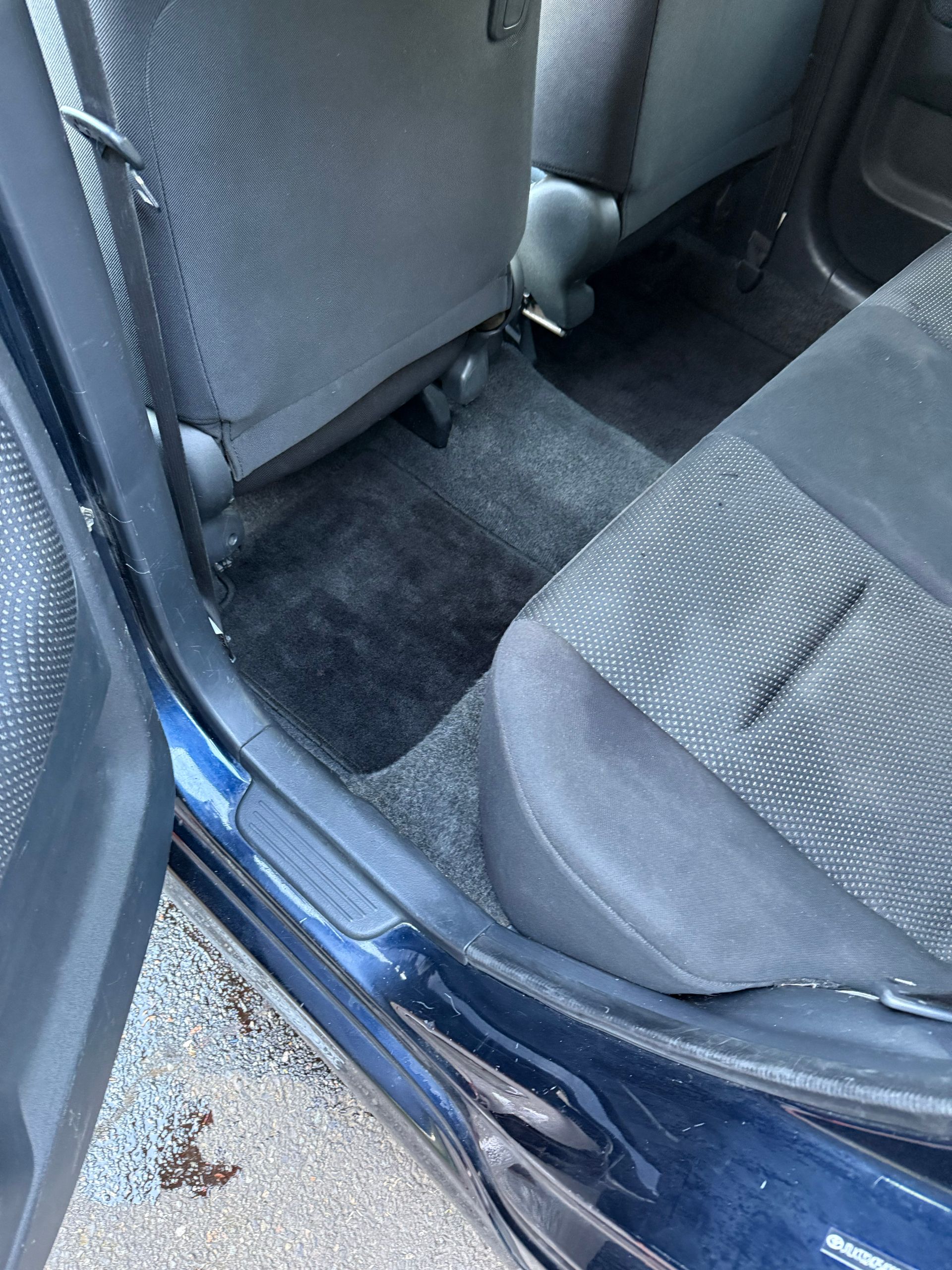 Car interior with rear seat upholstery and a blue door sill, viewed from outside.