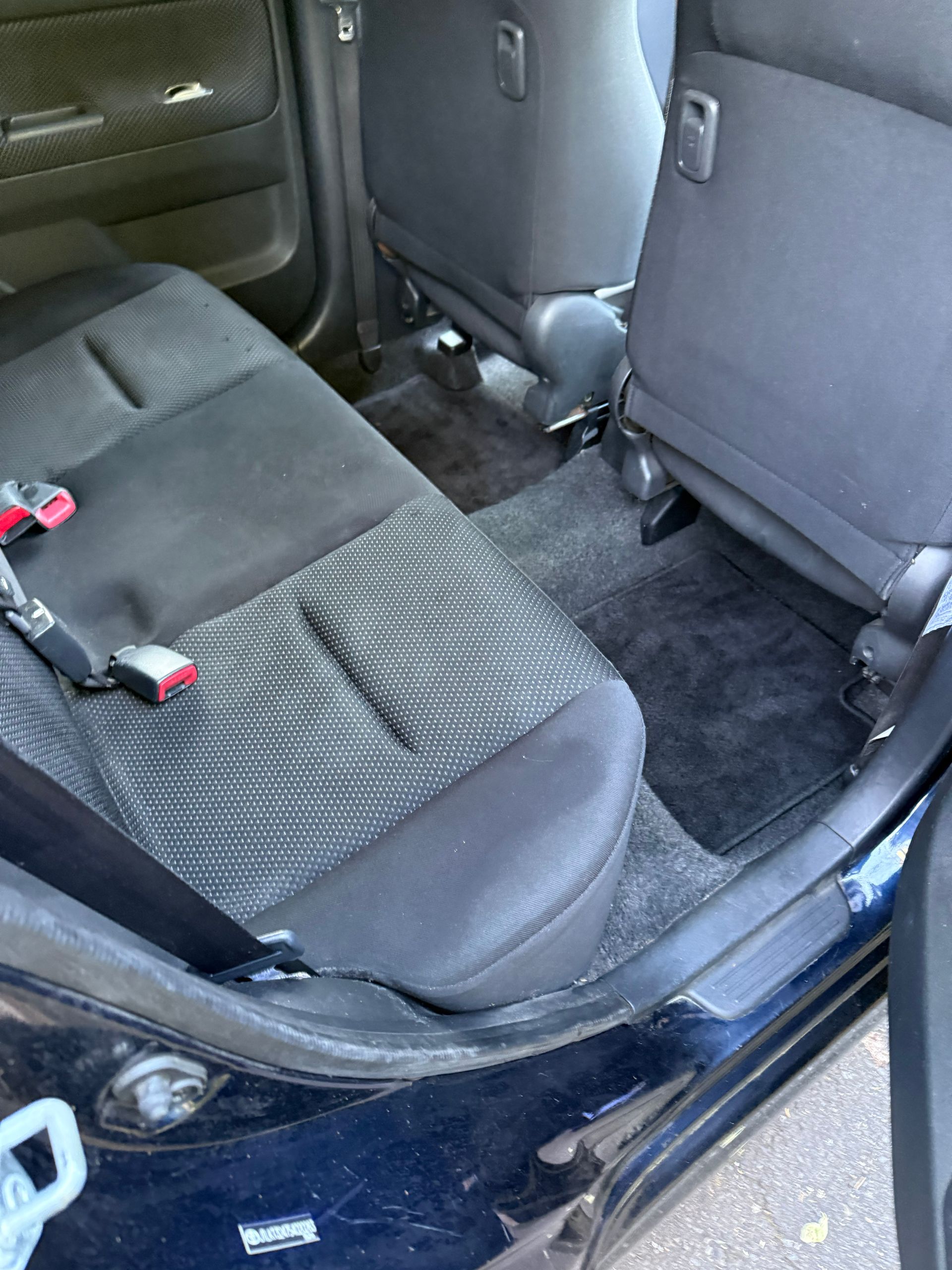Car back seat with folded rear seat, dark upholstery, and seat belts visible