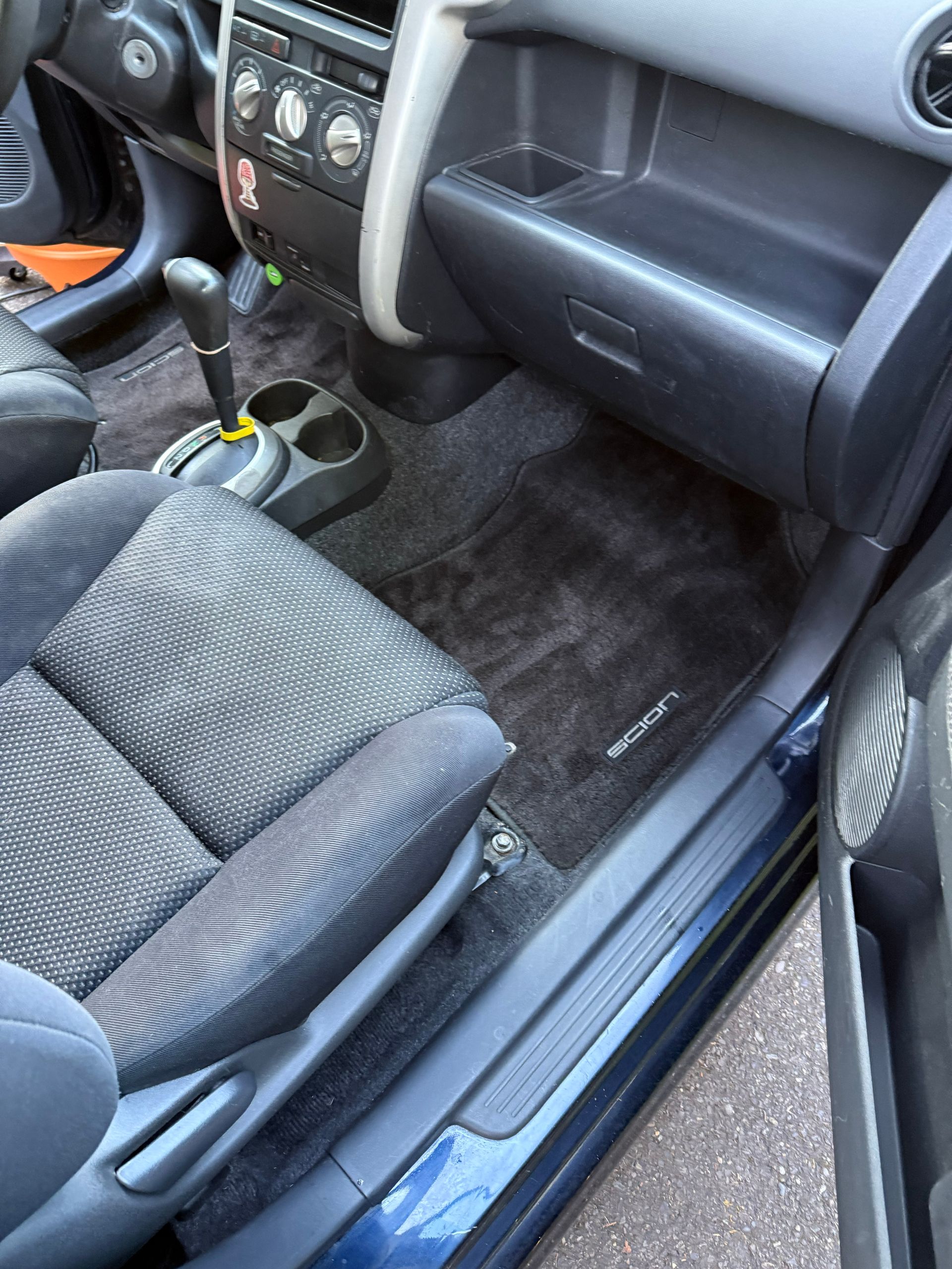 Car interior with front passenger seat, center console, and floor mat visible, showing some dust and wear