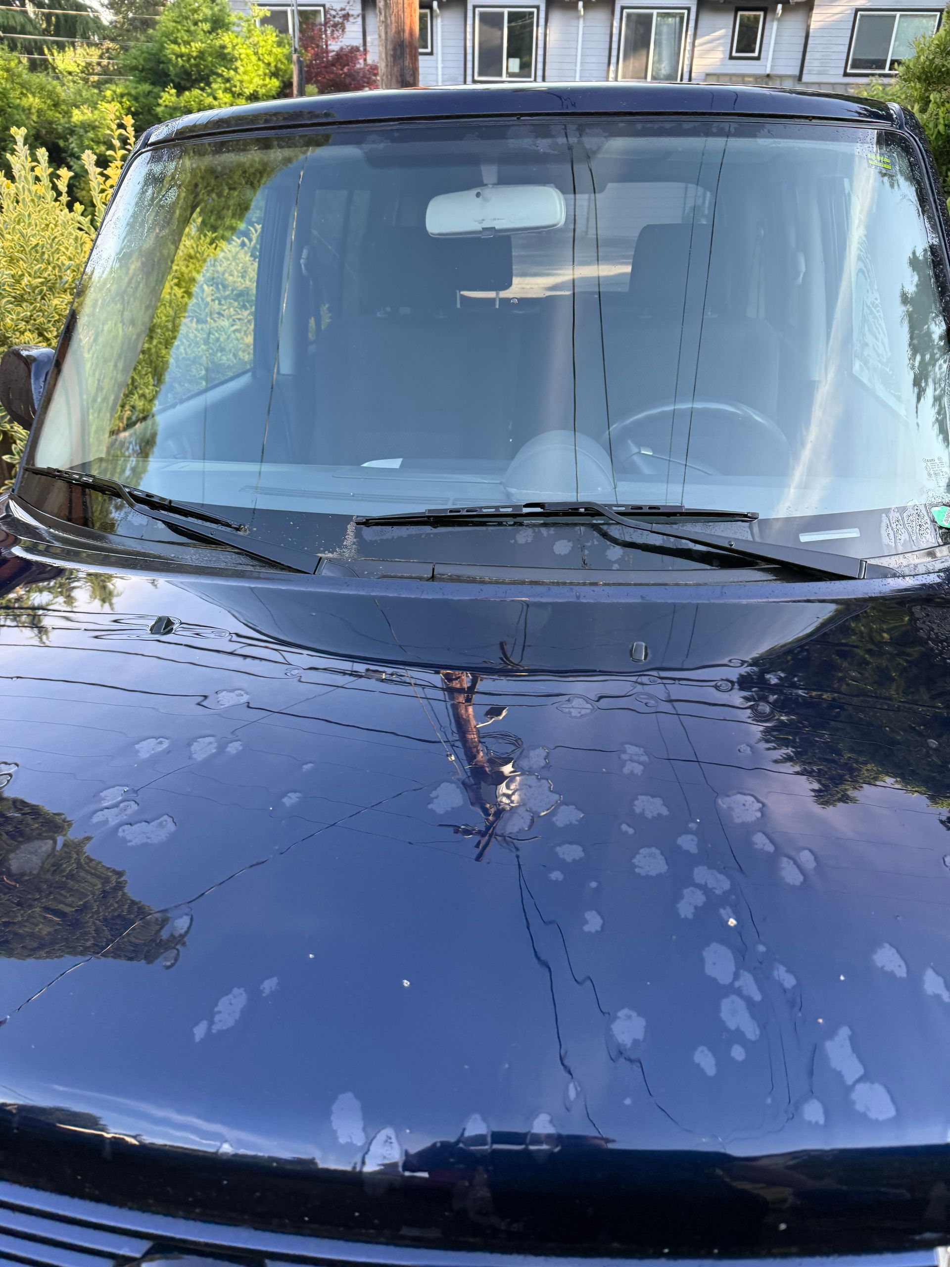 Dark blue car front with rain droplets parked in a driveway, house reflected on windshield