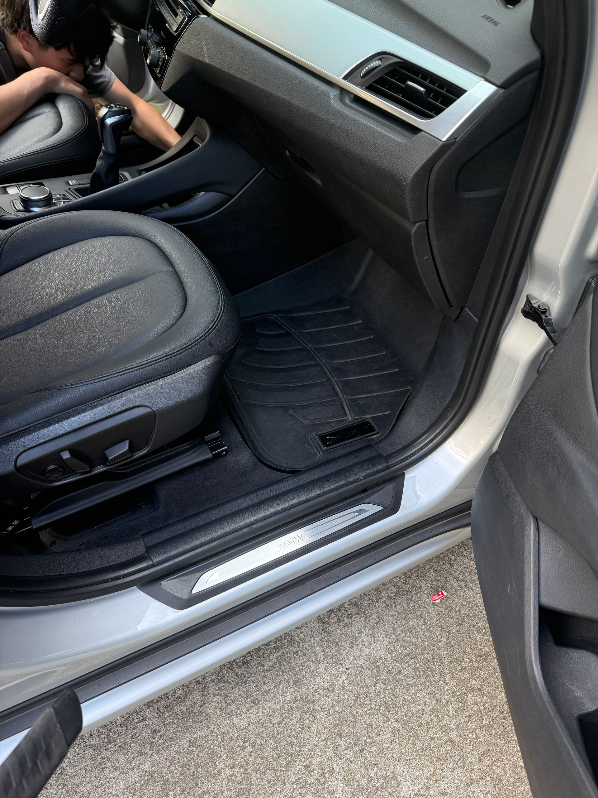 Car interior with open passenger door, black floor mat, and a child seat visible in the back.