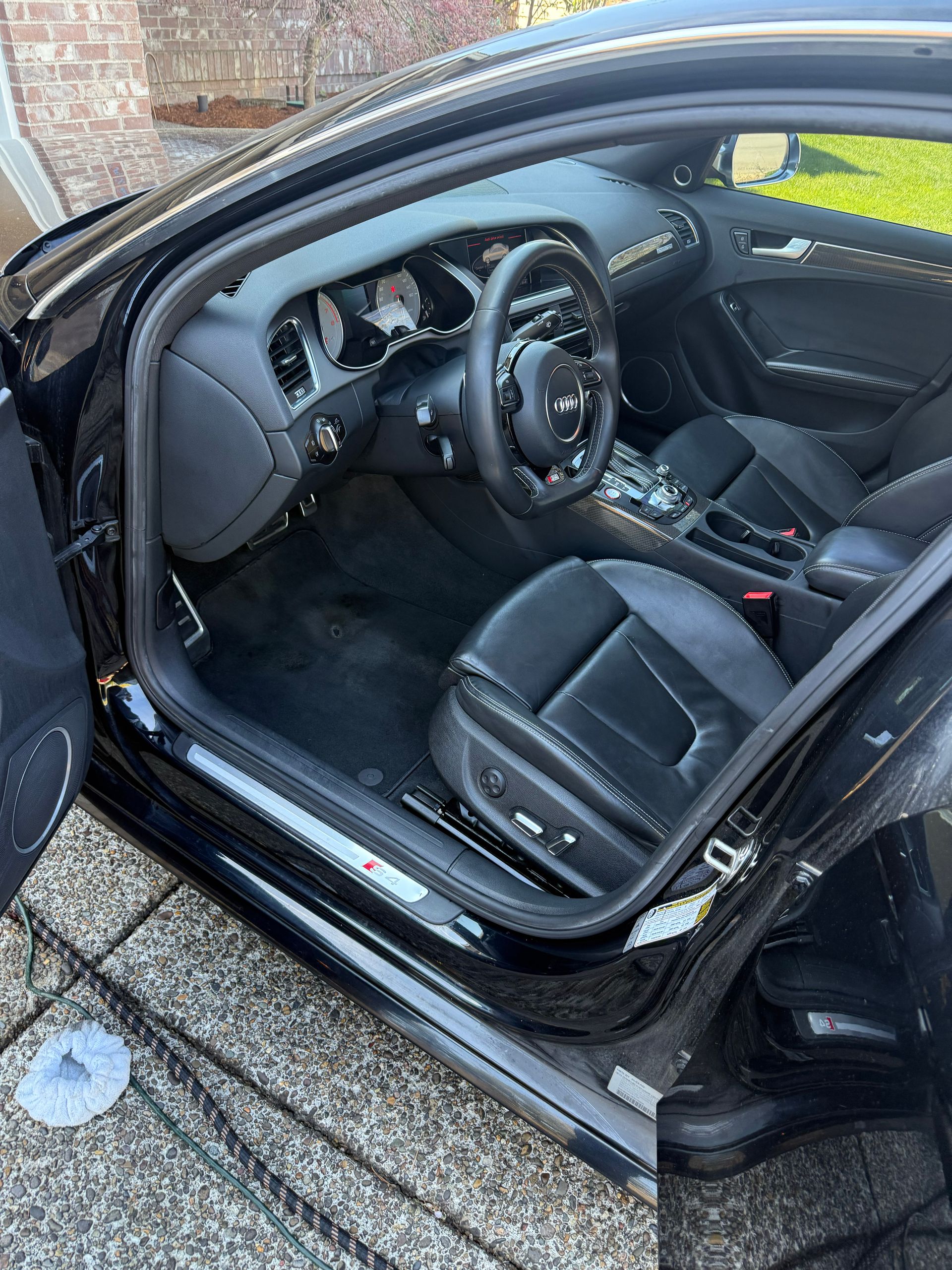 Open car door showing a black leather driver’s seat and dashboard interior.