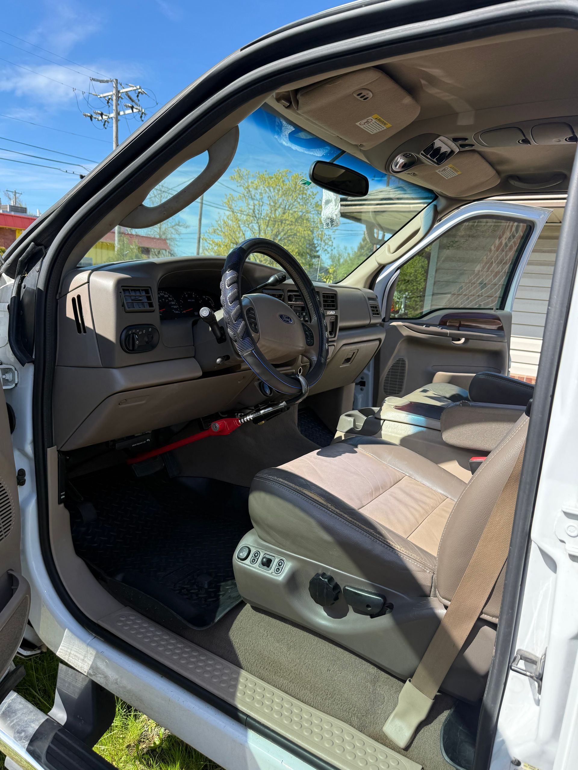 Open SUV driver’s door showing tan leather interior, steering wheel, and dashboard in daylight.