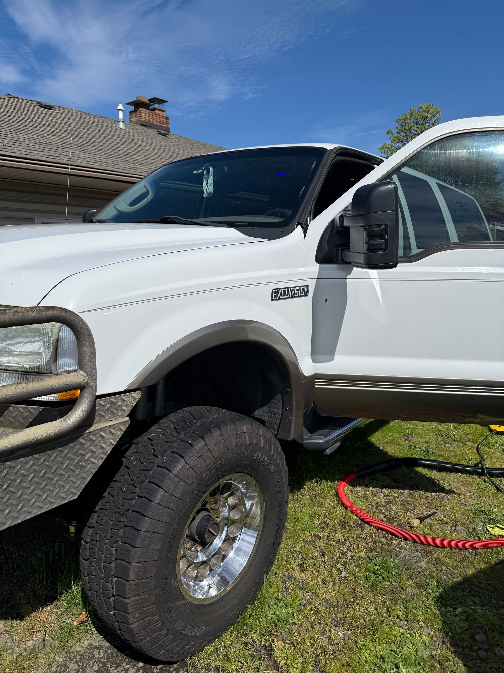 White lifted pickup truck in a driveway, front side view with open driver door and large off-road tires.
